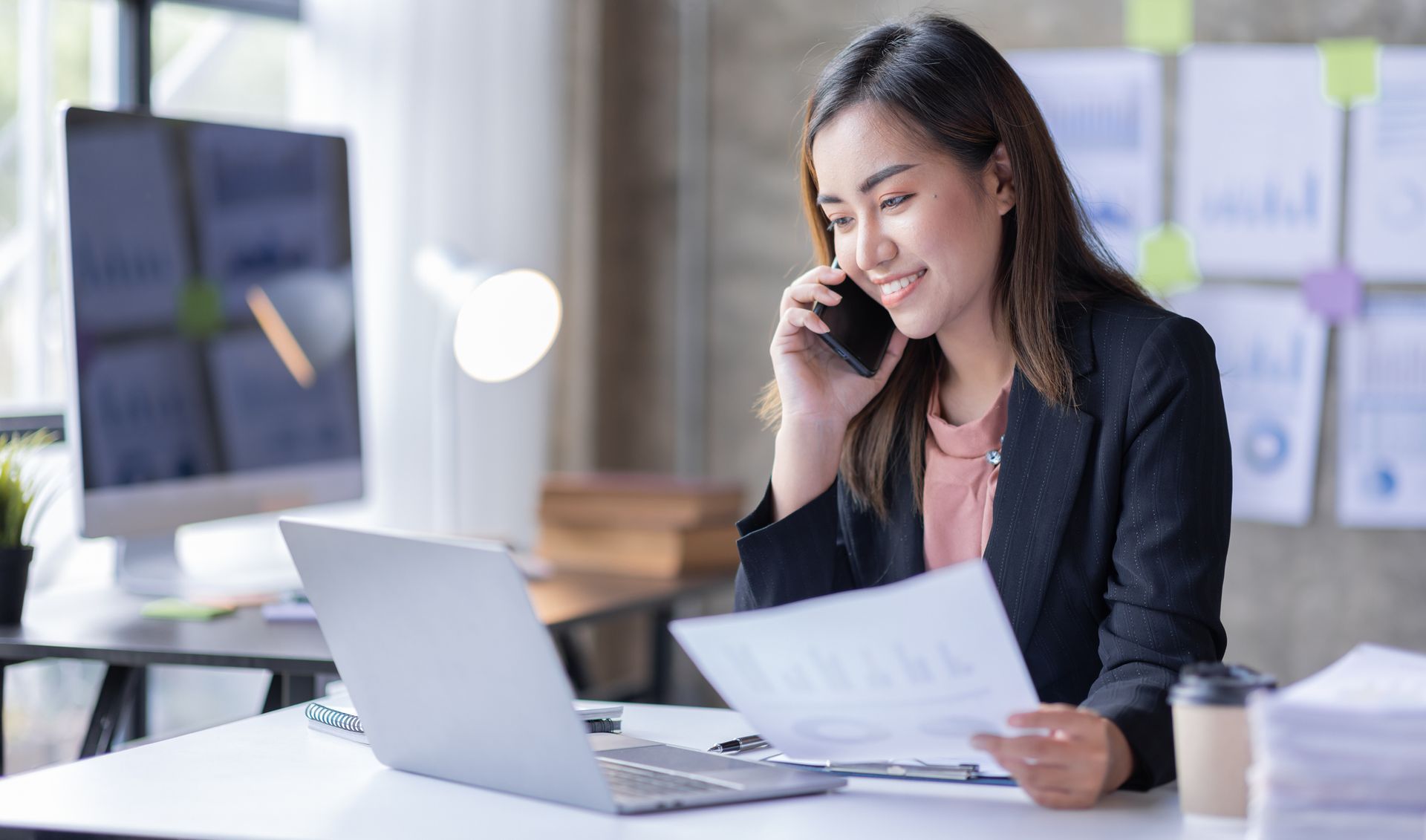 A woman is sitting at a desk talking on a cell phone.