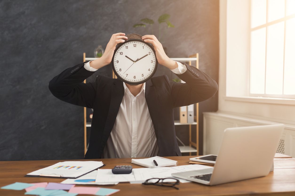 A man is sitting at a desk with a clock in front of his face.