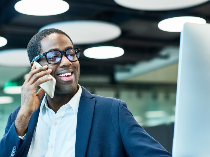 A man in a suit is talking on a cell phone in front of a computer.