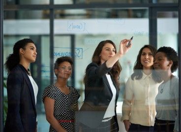 A group of women are standing around a glass wall.
