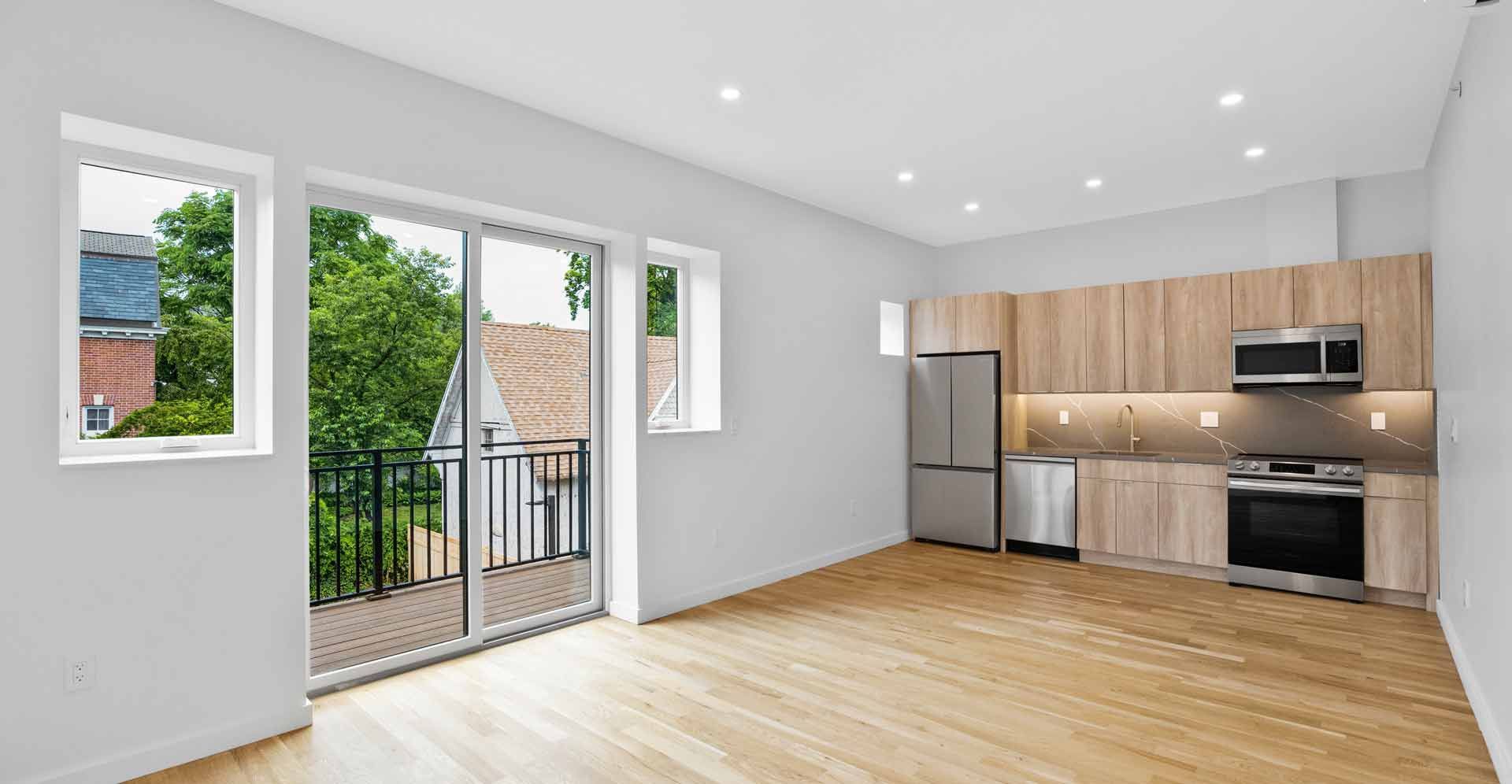 An empty living room with a kitchen and a balcony.