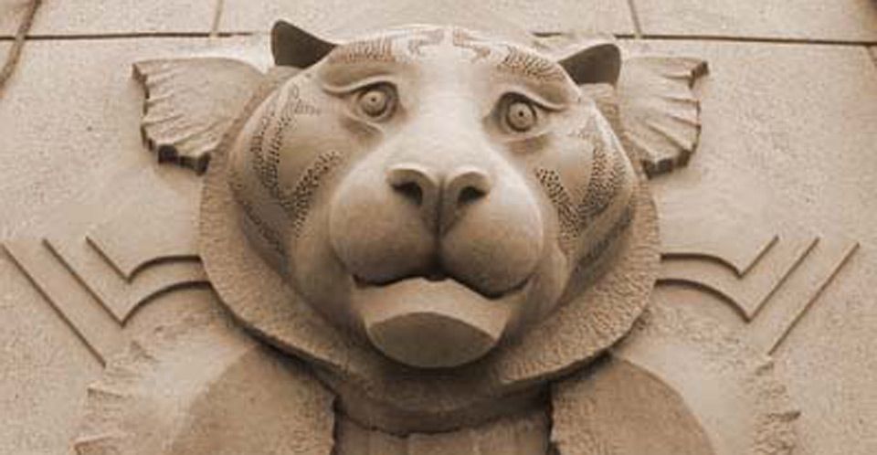 A statue of a tiger 's head is carved into the side of a building.