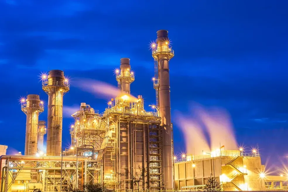 A large industrial plant is lit up at night with smoke coming out of the chimneys.