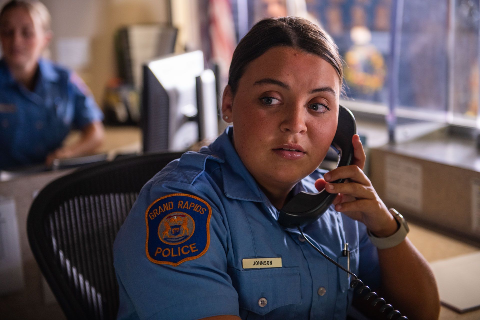 Police officer at desk on phone.