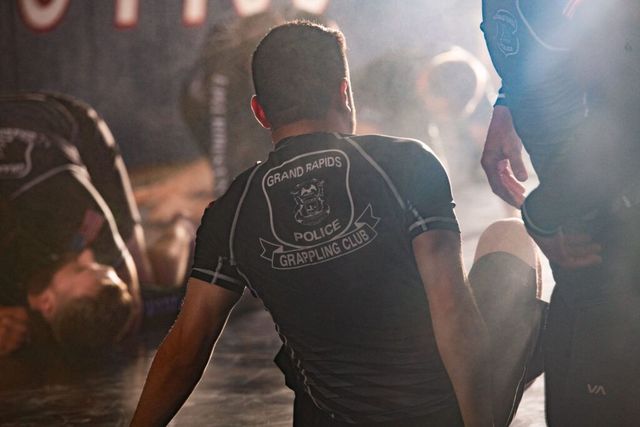 People in a martial arts class, one with a Police logo on their shirt, training on the floor.