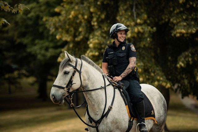 Police officer on horseback, smiles, rides through a park.