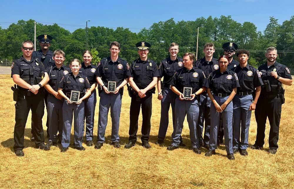 Police officers in uniform standing outside, holding plaques, smiling.