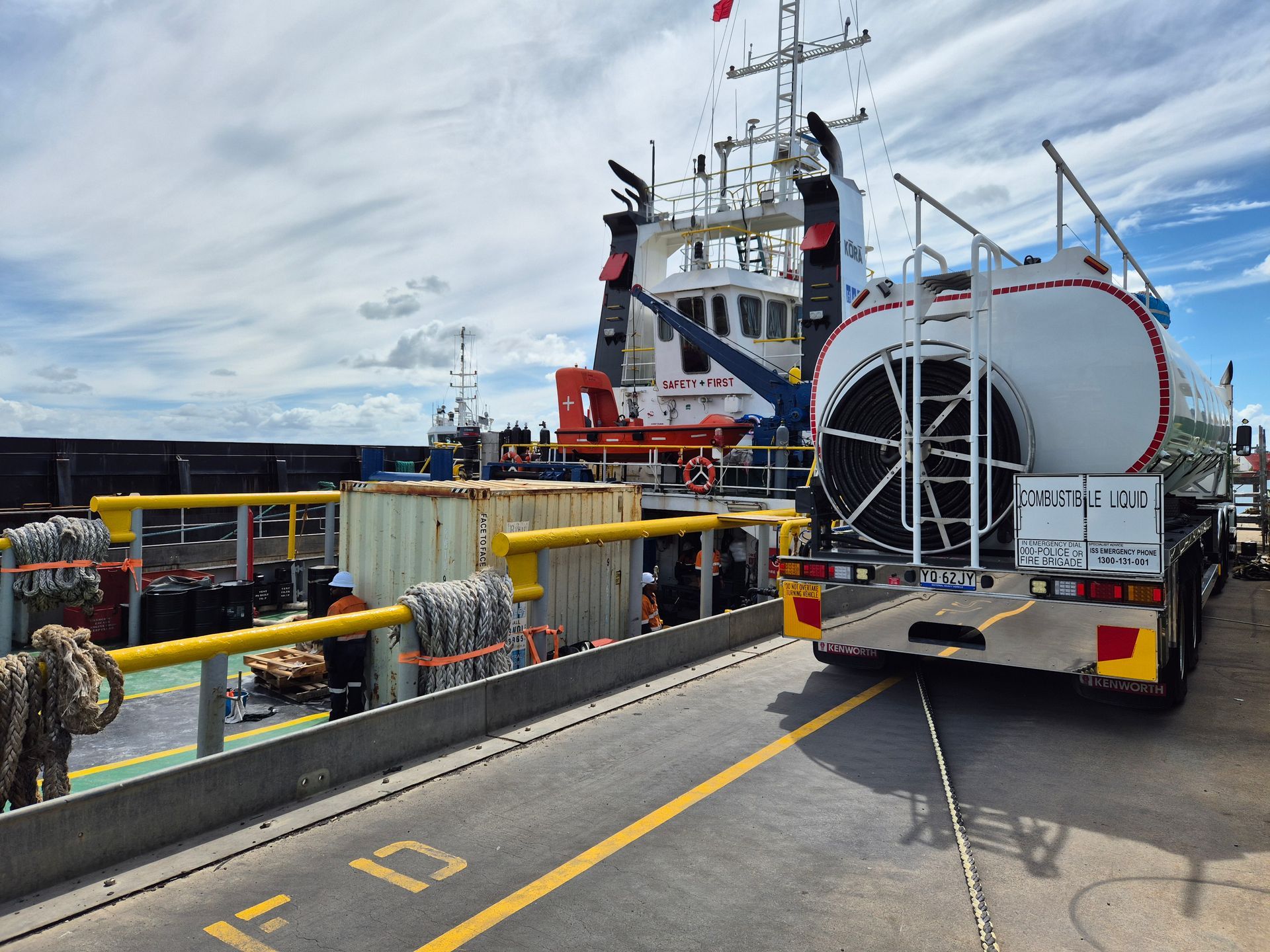 Large white cylindrical cargo loaded on a ferry beside a dock with safety railings and workers nearby
