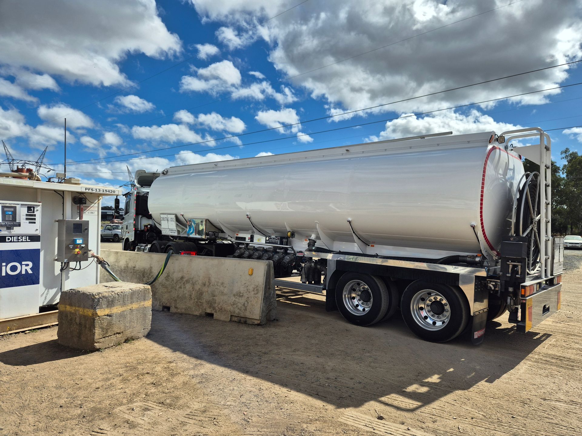 Silver tanker trailer parked on a dirt lot under a cloudy blue sky