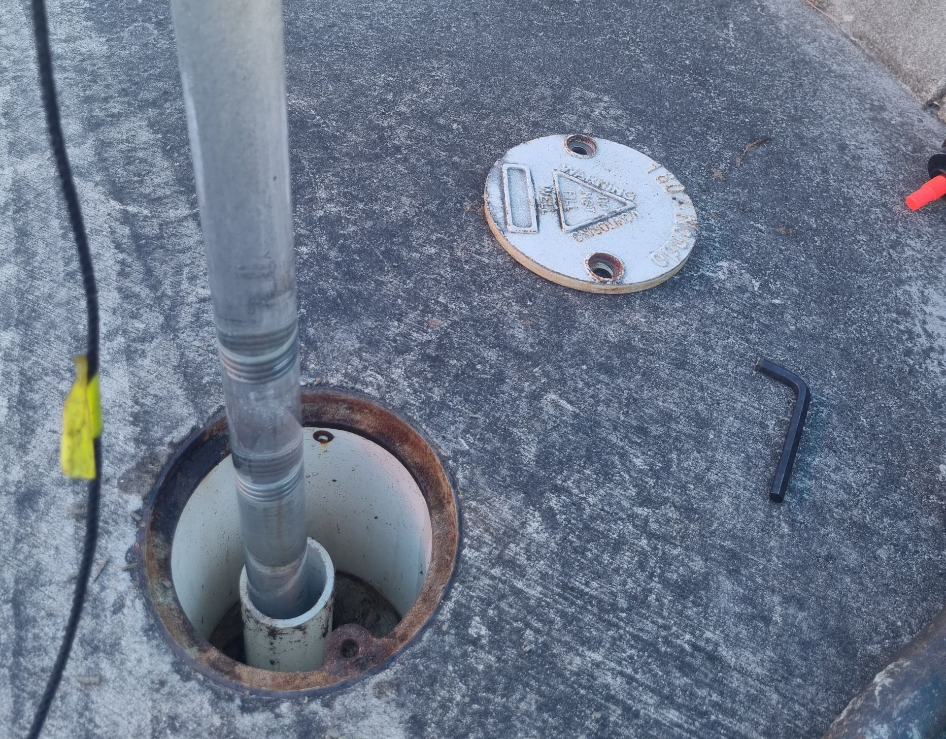 Roof vent pipe in a circular opening beside a white access cap on a gravel-covered roof.