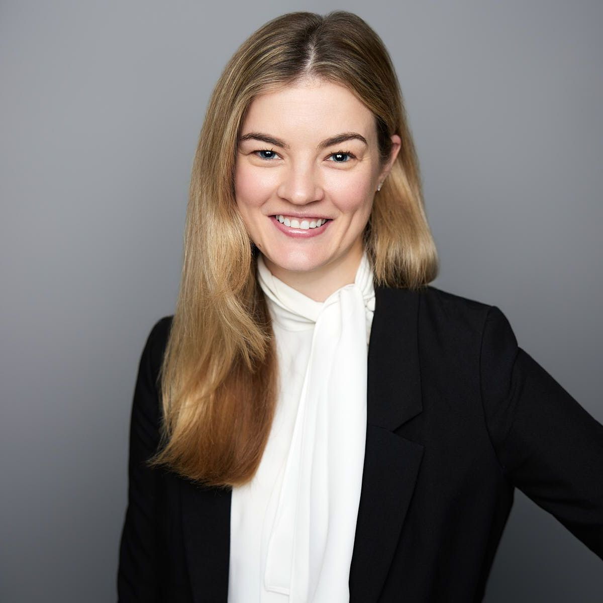 A woman wearing a black jacket and a white shirt is smiling for the camera.