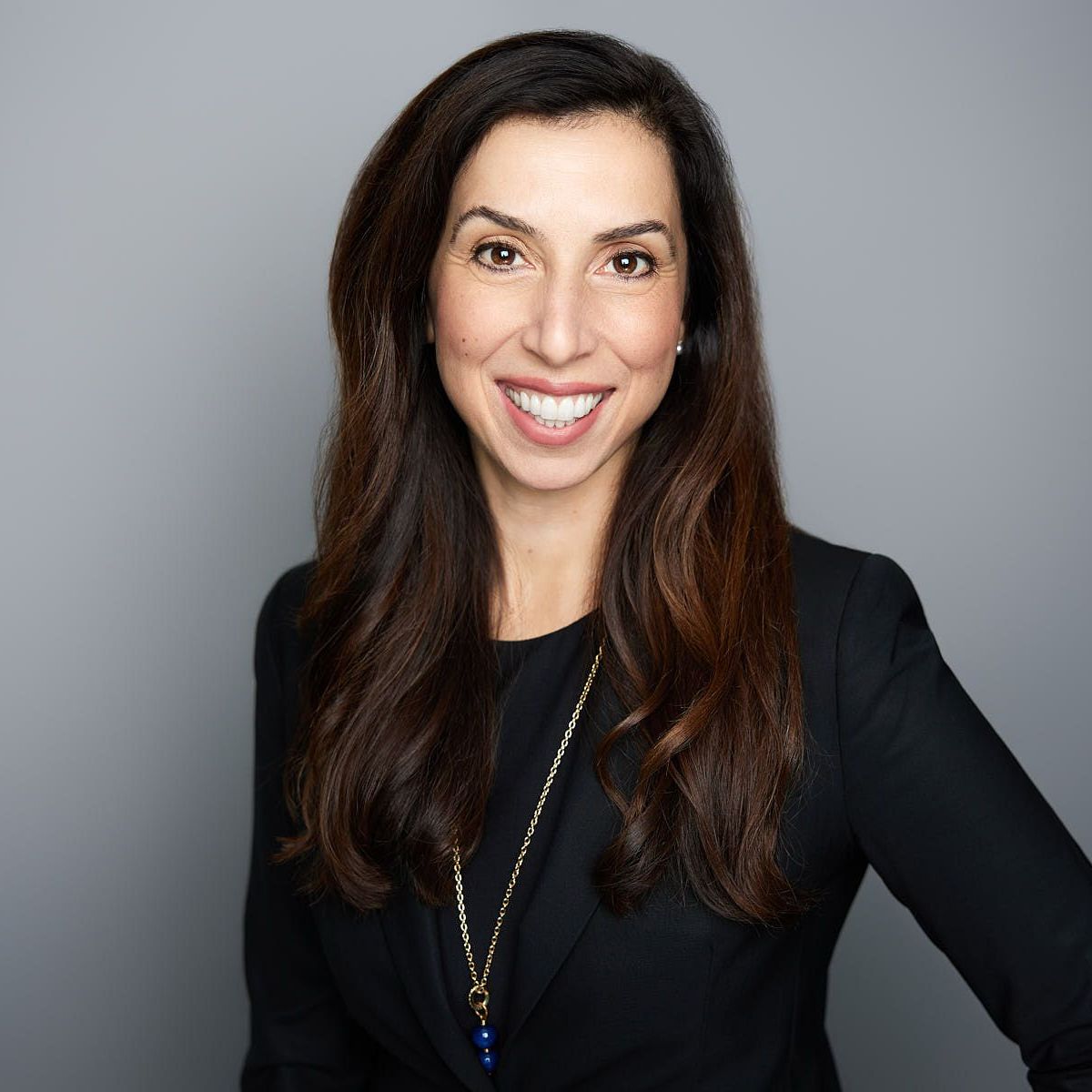 A woman wearing a black jacket and a necklace is smiling for the camera.