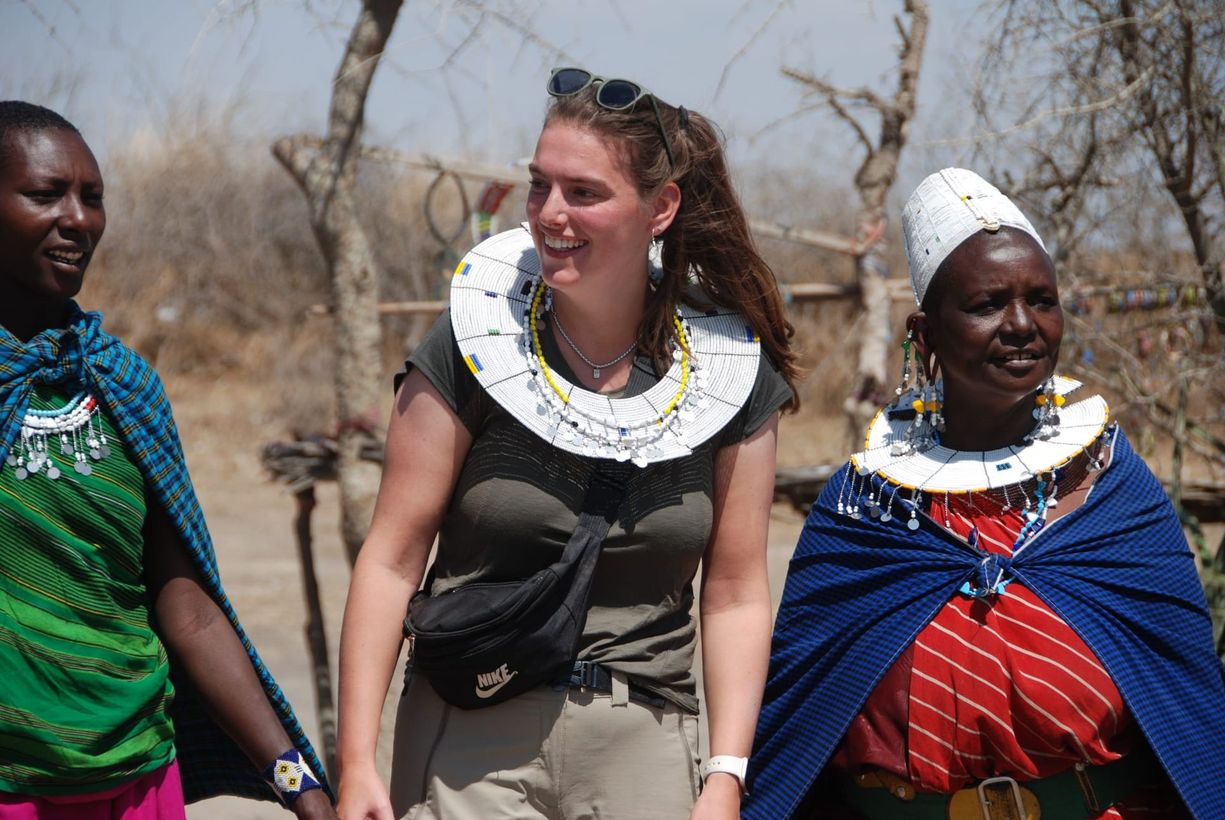 Three people walking outdoors, wearing colorful beaded necklaces and traditional clothing