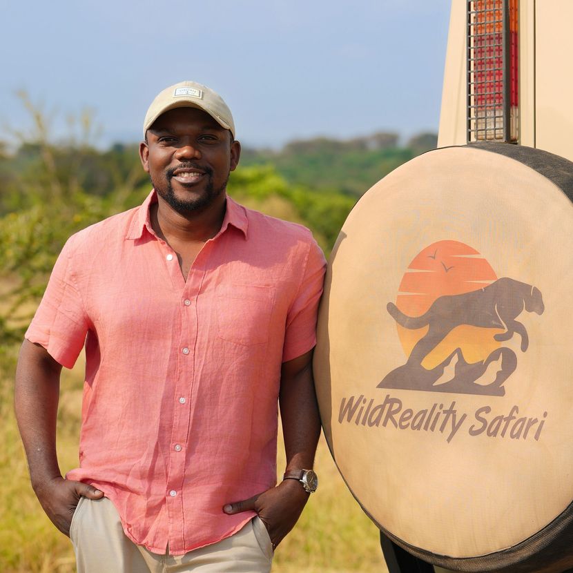 Man in a pink shirt standing beside a WildReality Safari sign in a sunny outdoor setting