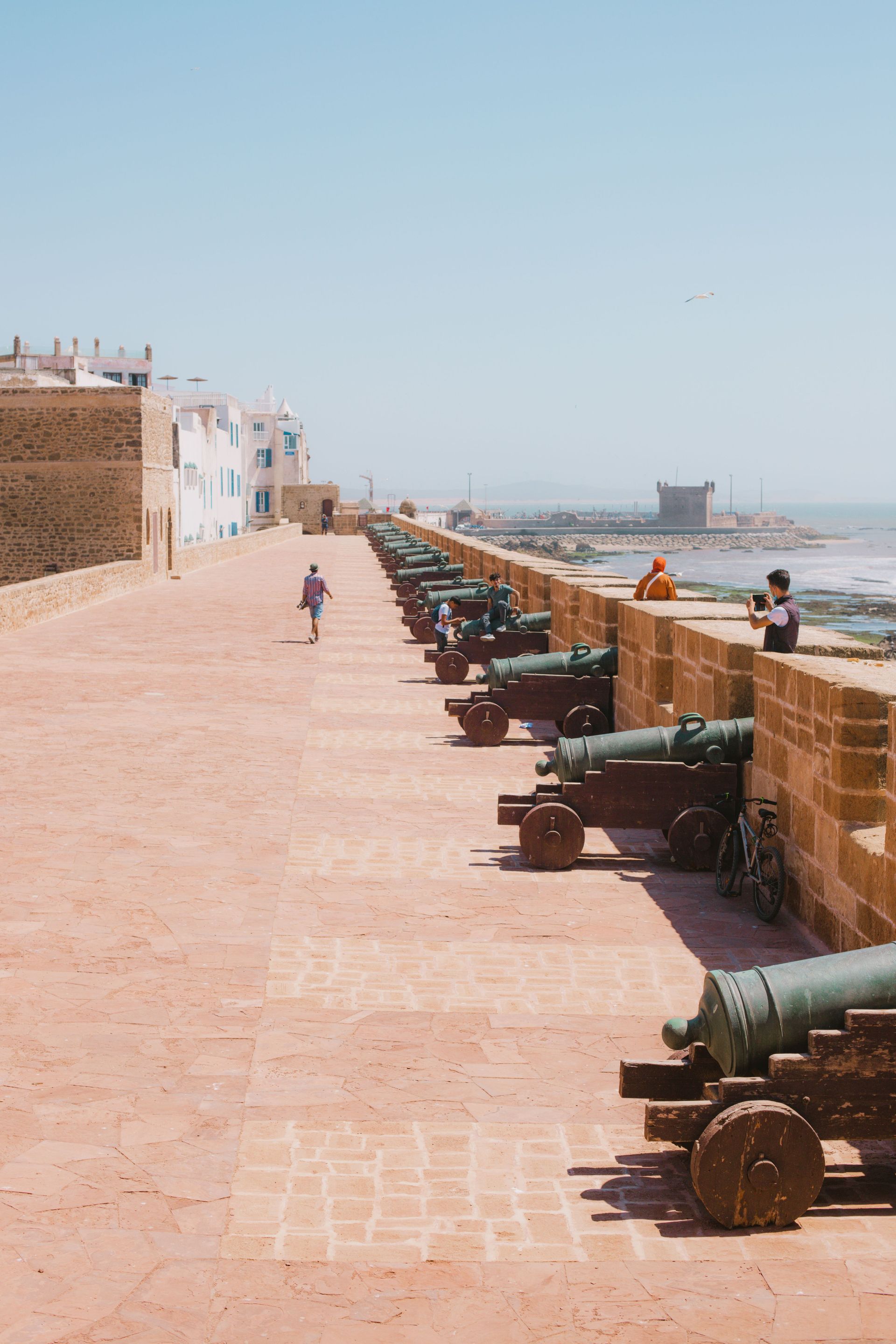 Seaside promenade with old cannons along a brick wall under a clear blue sky