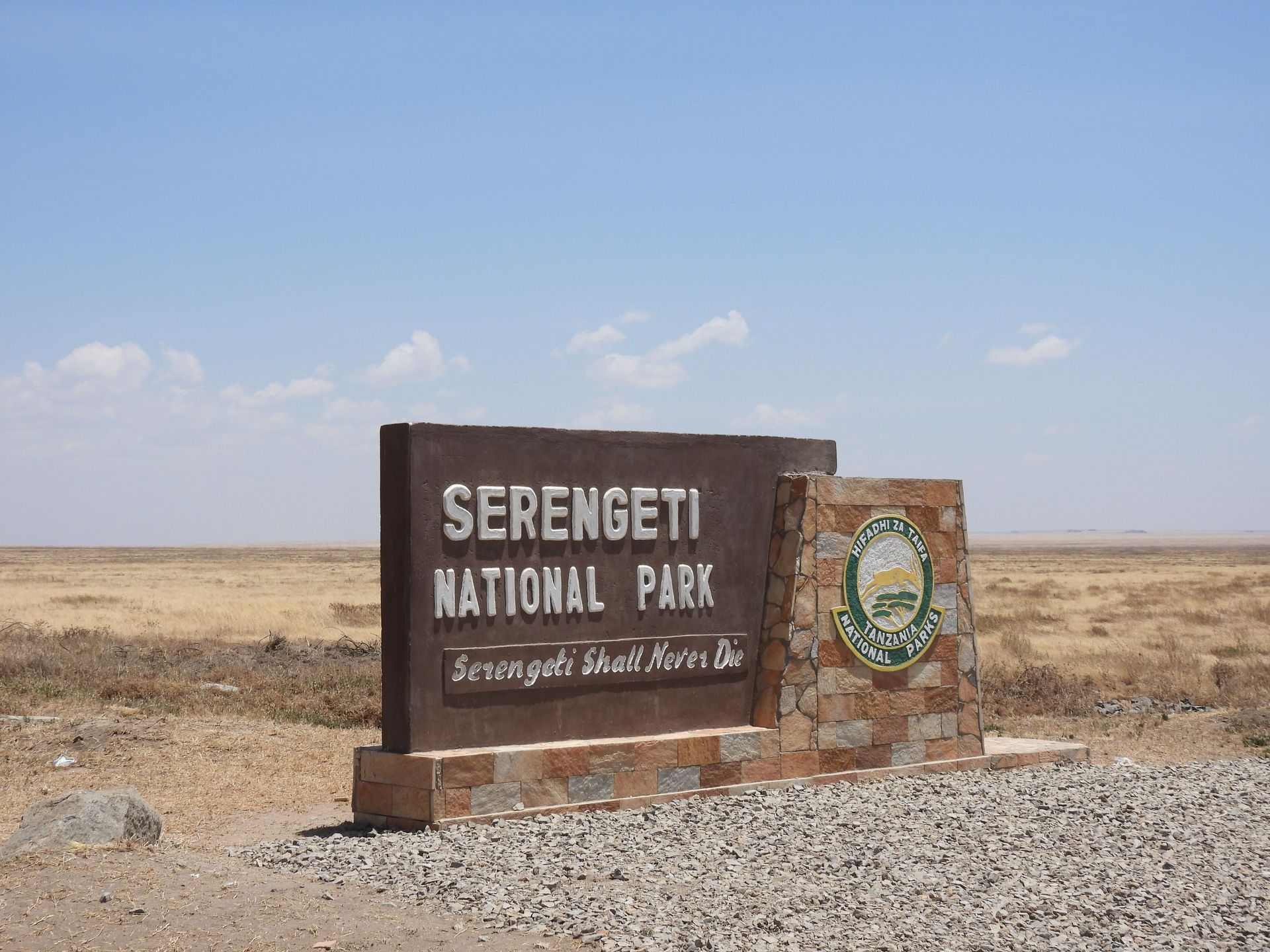 Serengeti National Park entrance sign beside a gravel road under a clear blue sky