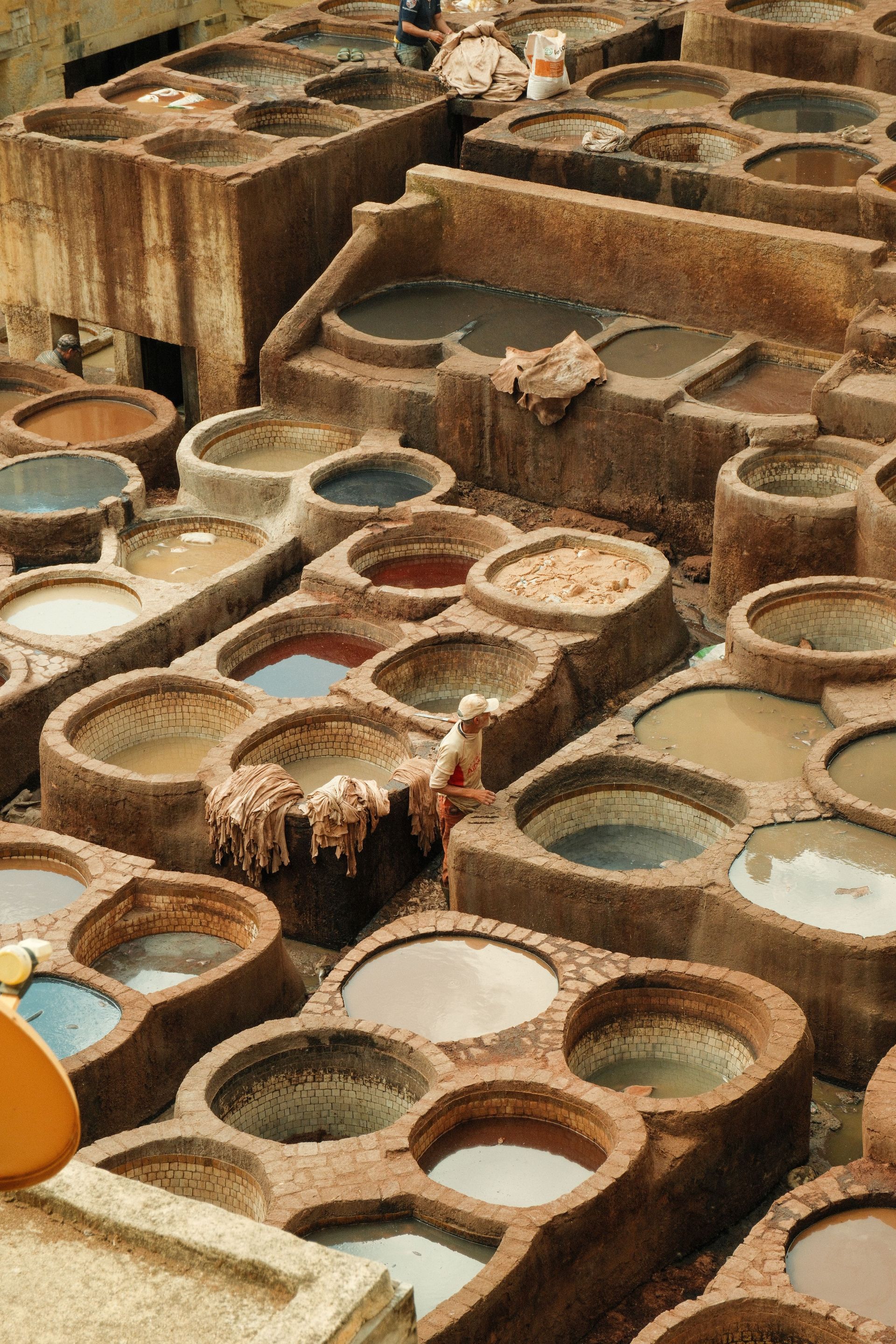 Rows of round clay dye vats in earthy reds, browns, and blues at a traditional textile workshop