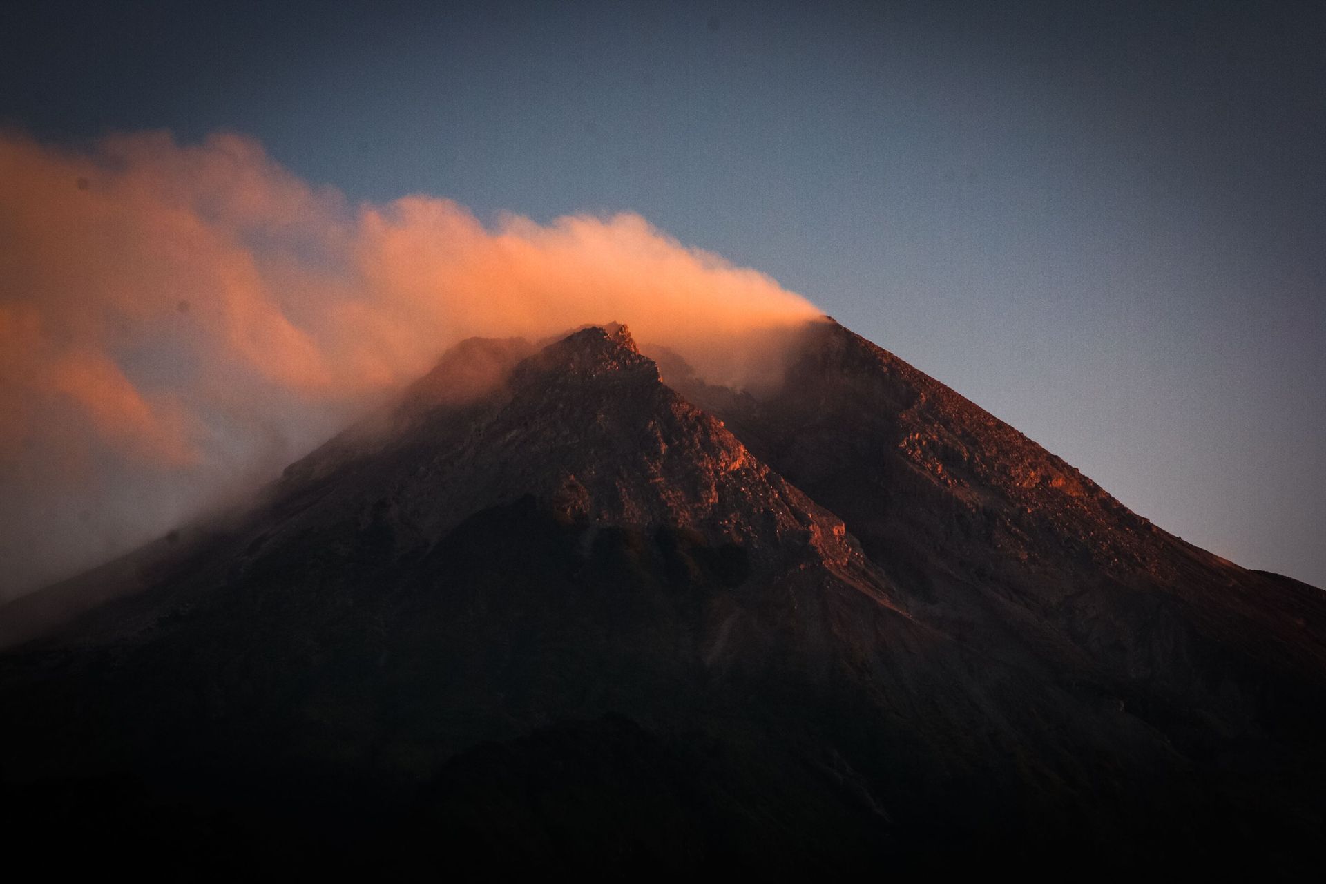 Volcanic mountain peak at dusk, with orange clouds glowing above the dark slopes.