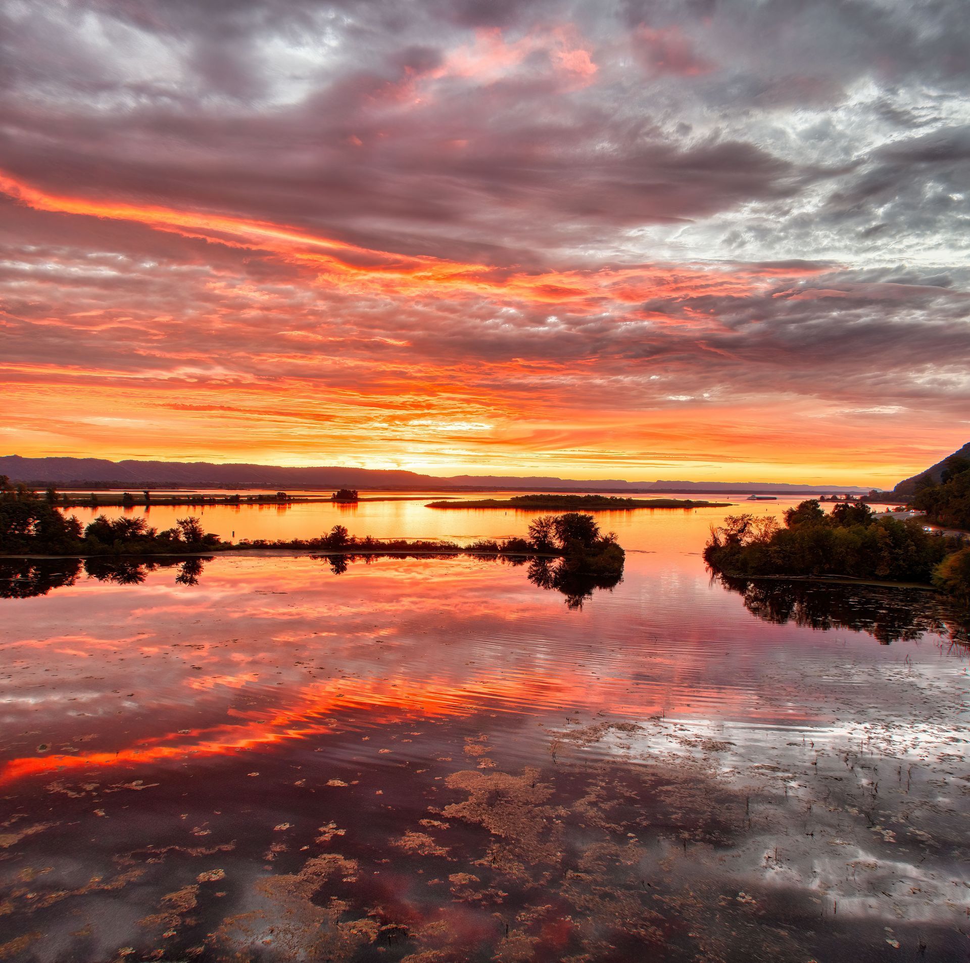 Fiery sunset over calm water with dramatic clouds and glowing reflections.