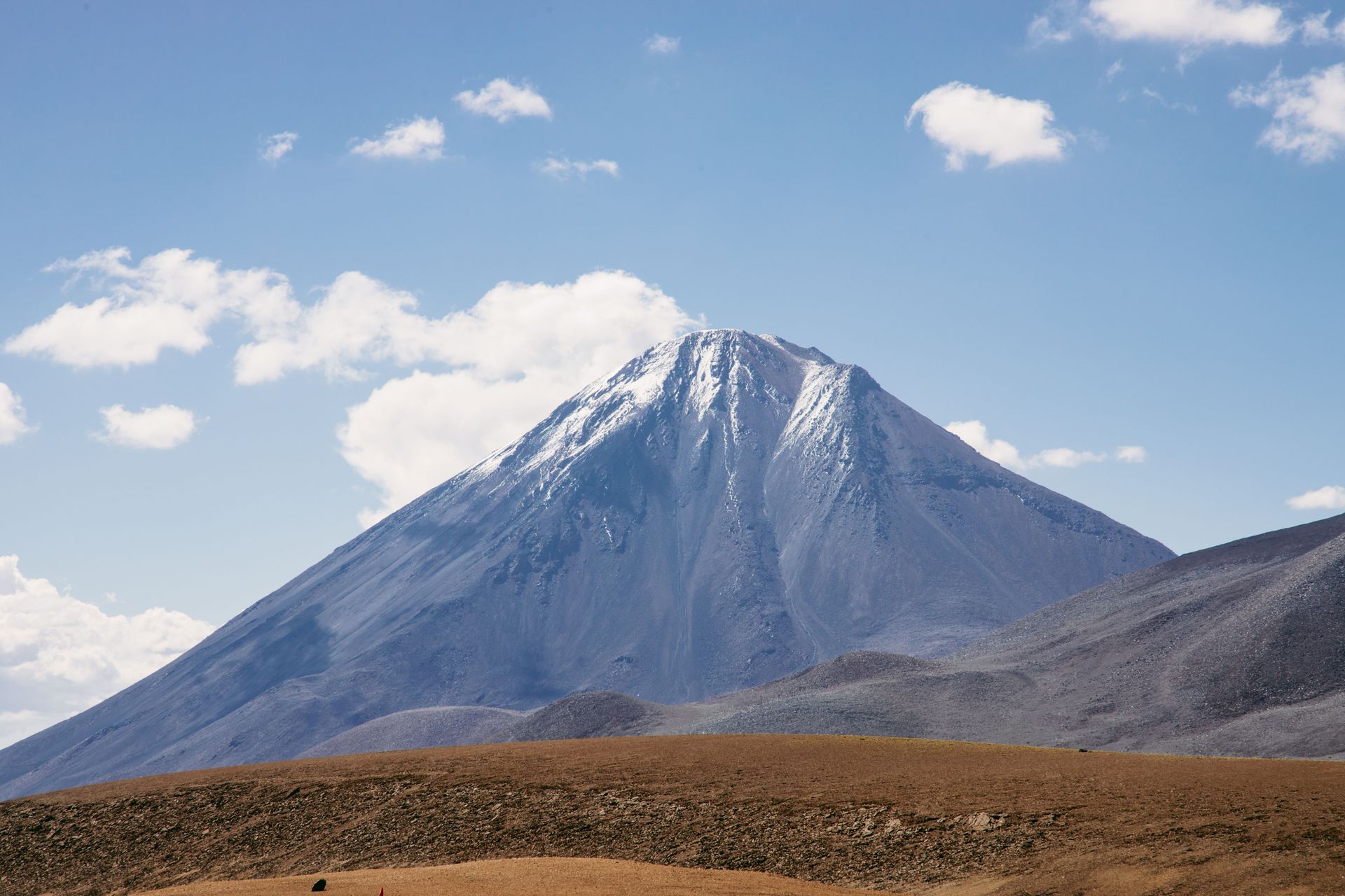 Snow-capped volcanic mountain under a blue sky above a brown plain