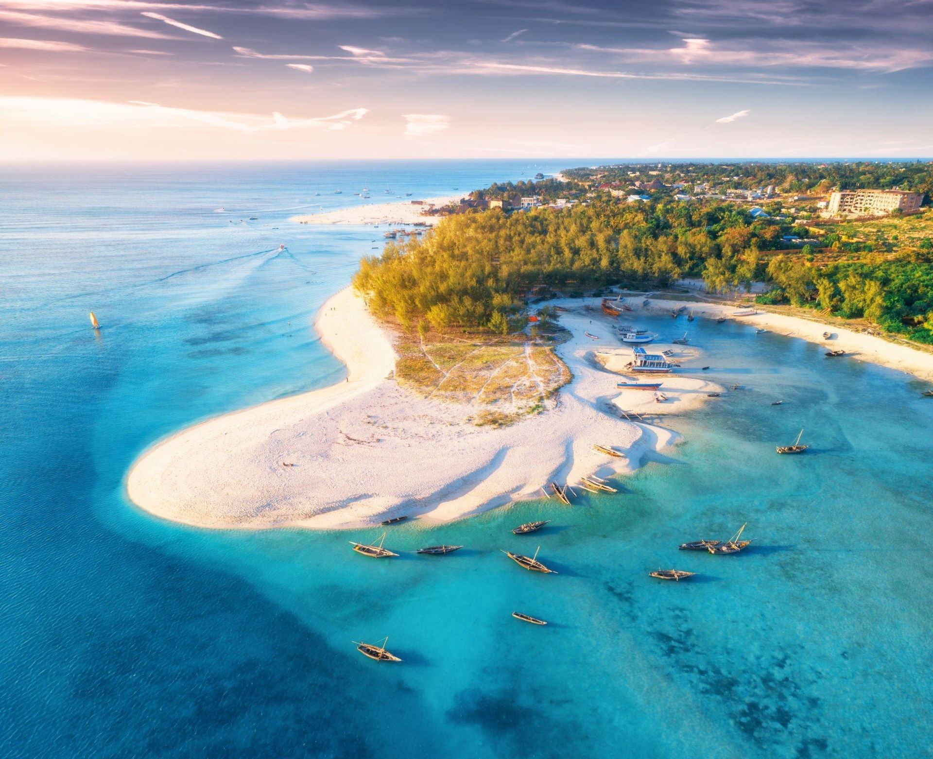 Aerial view of a tropical beach with turquoise water, white sand, and boats near a lush coastline.