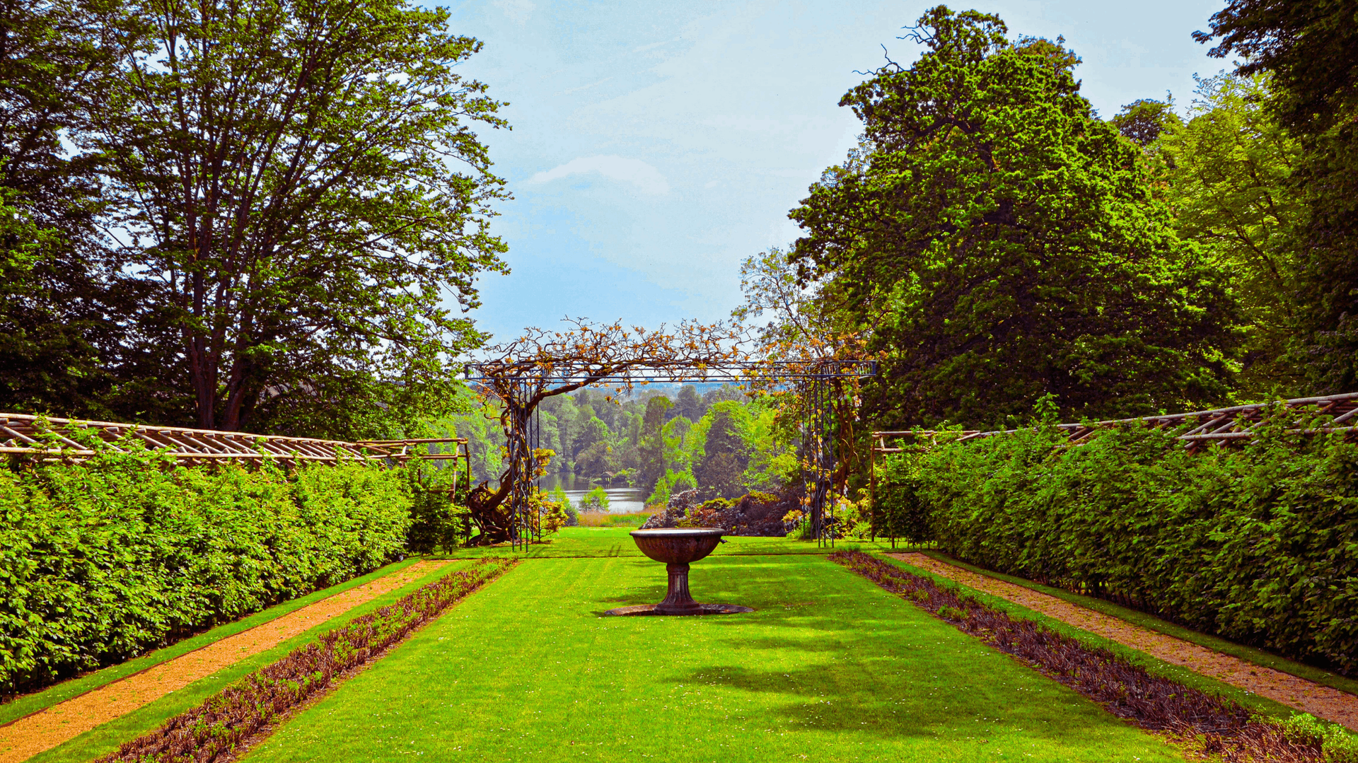 Lush green garden with manicured hedges, a bird bath, and trees under a blue sky — Rohan's Maintenance in Robina, QLD