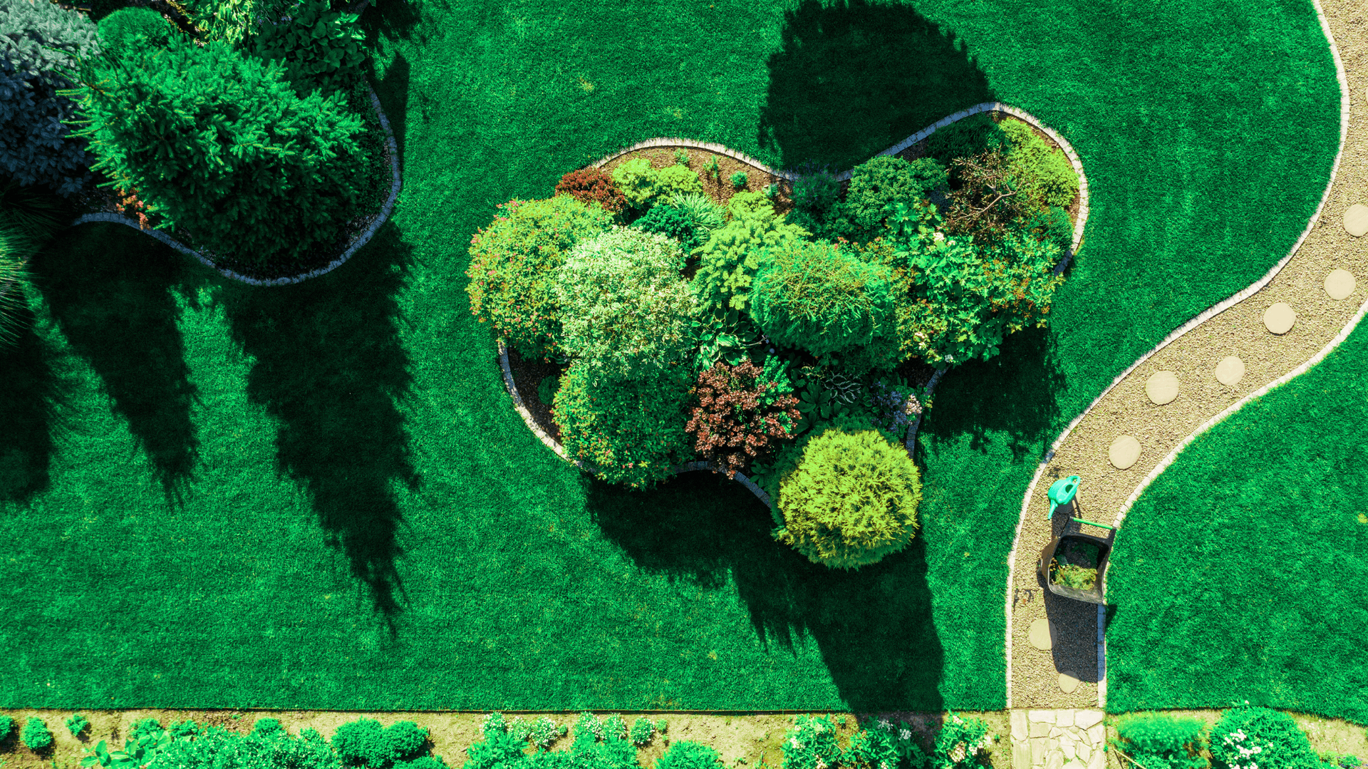 Overhead view of a lush garden with a winding stone path, surrounded by green grass and colorful plants — Rohan's Maintenance in Robina, QLD