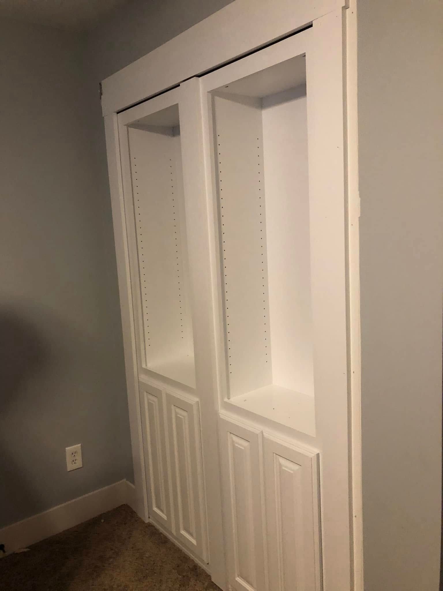 White built-in closet with open shelves in a beige room with carpet and a wall outlet.