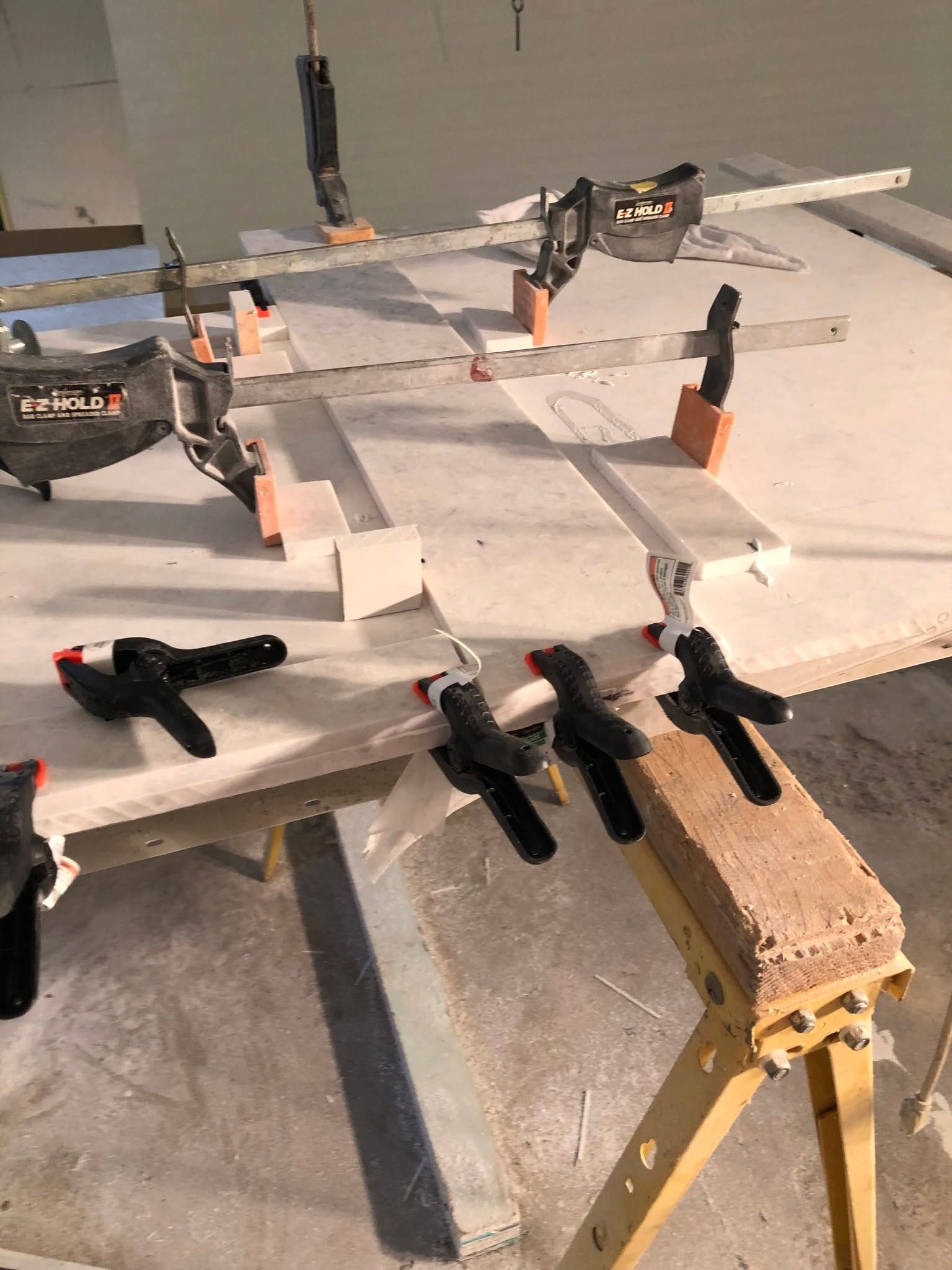 Clamps hold white foam boards on a workbench in a workshop setting.