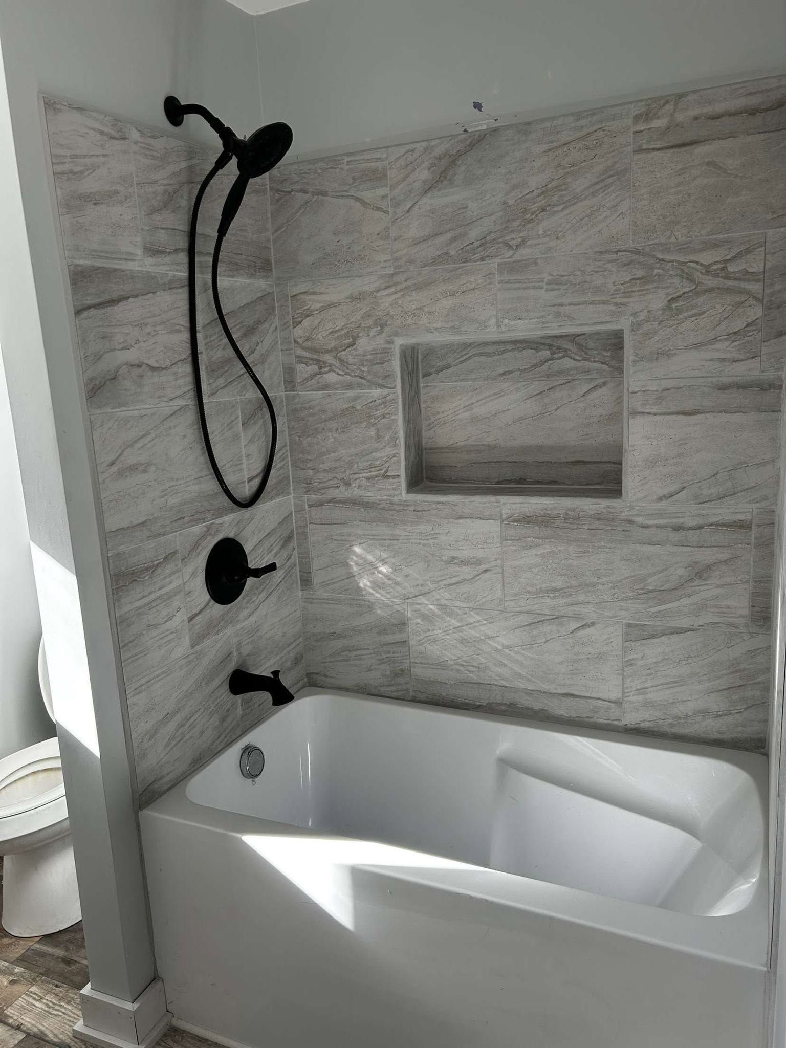 Modern bathroom with white soaking tub, black shower fixtures, and gray stone tile walls.