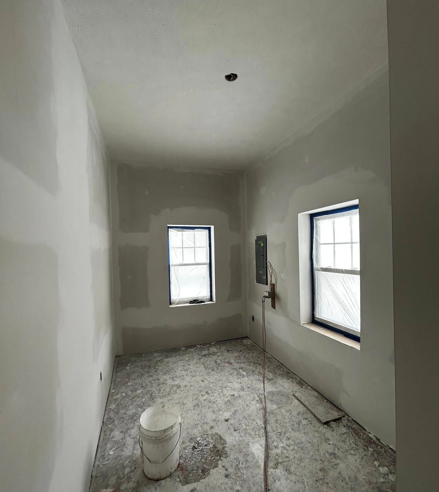 Small unfinished room with white walls, exposed floor, and two windows letting in daylight.
