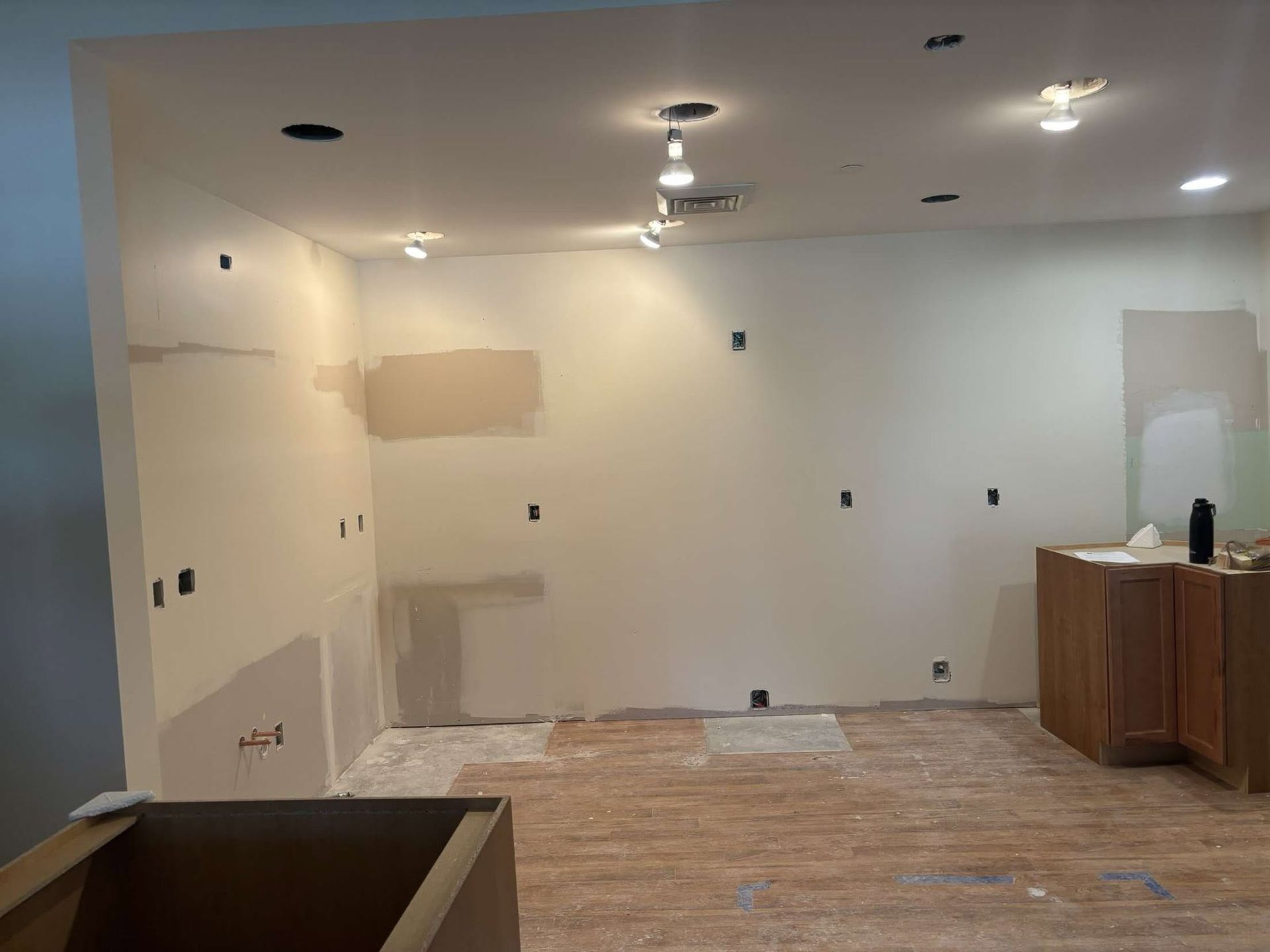 Renovated room with bare walls, ceiling lights, unfinished floor, and a vanity cabinet on the right