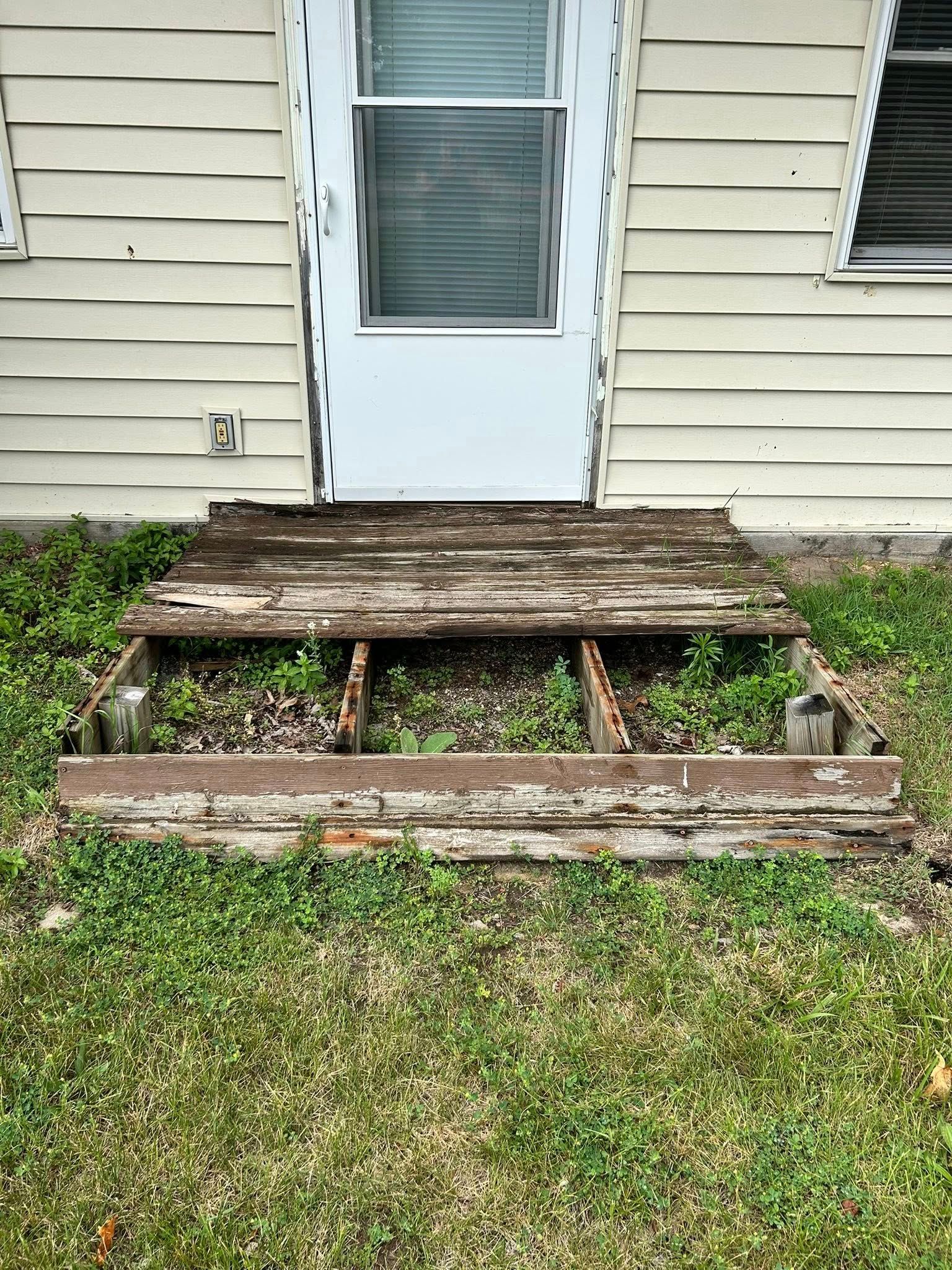 Damaged wooden front steps and planter bed in front of a white house door