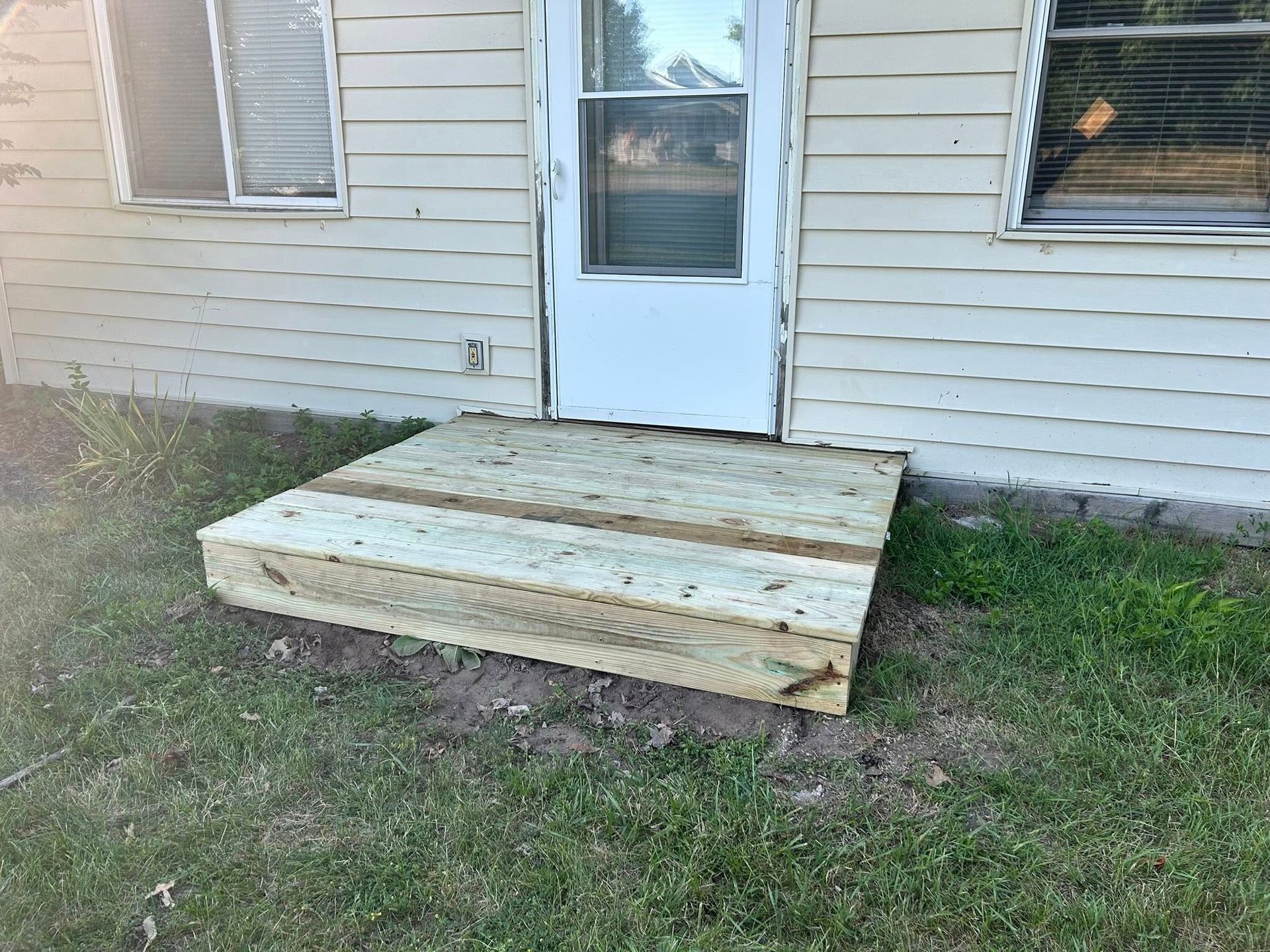 Wooden ramp leading to a white back door on a house with siding and grass in front