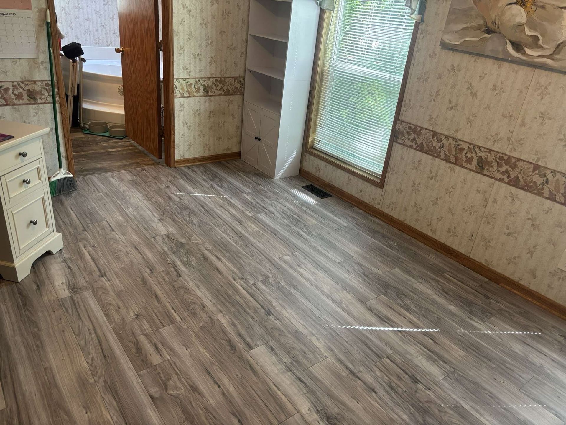 Empty room with wood-look flooring, beige walls, and a large window letting in light