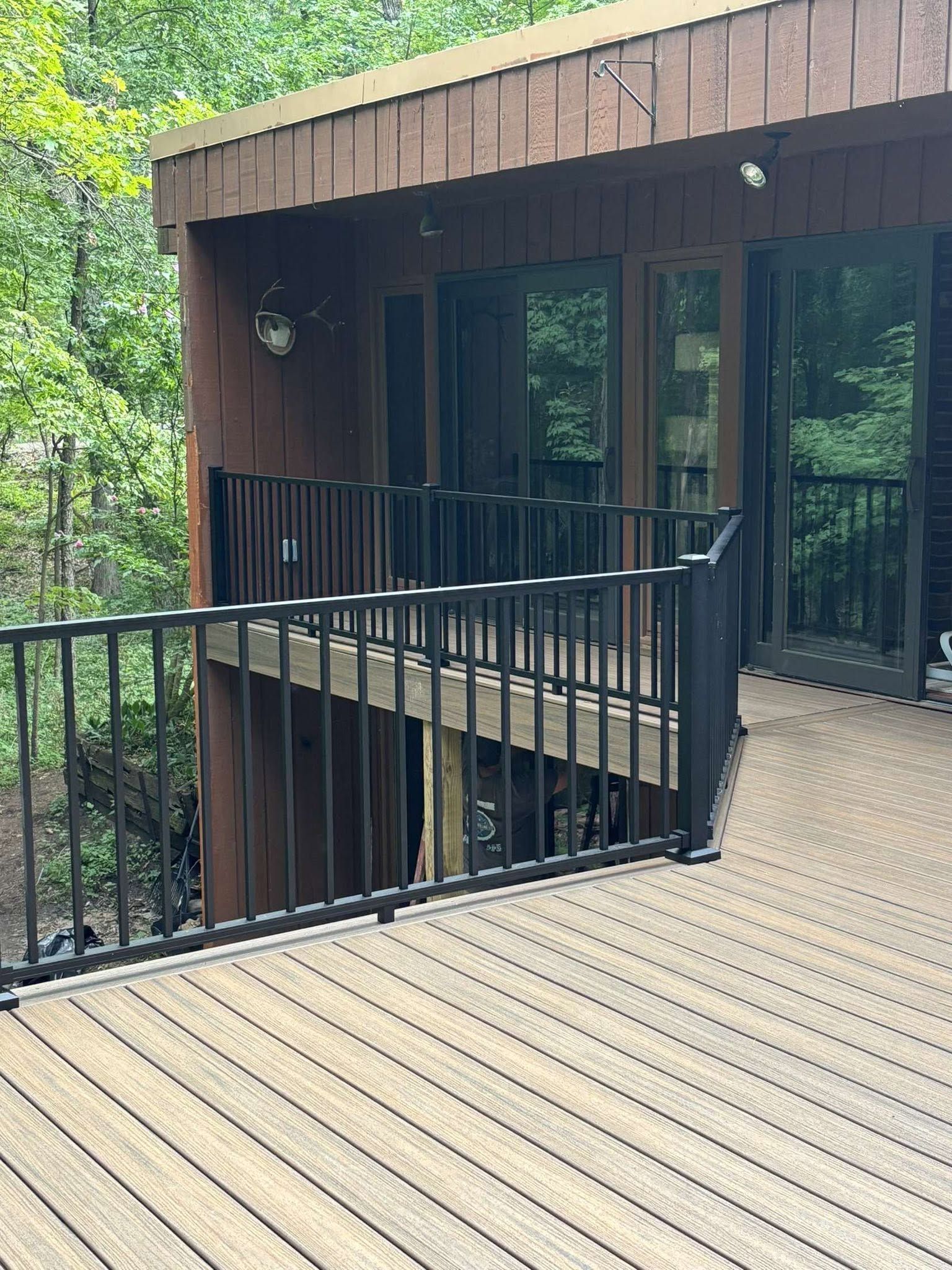 Wooden deck with black railing and sliding glass doors on a cabin surrounded by trees