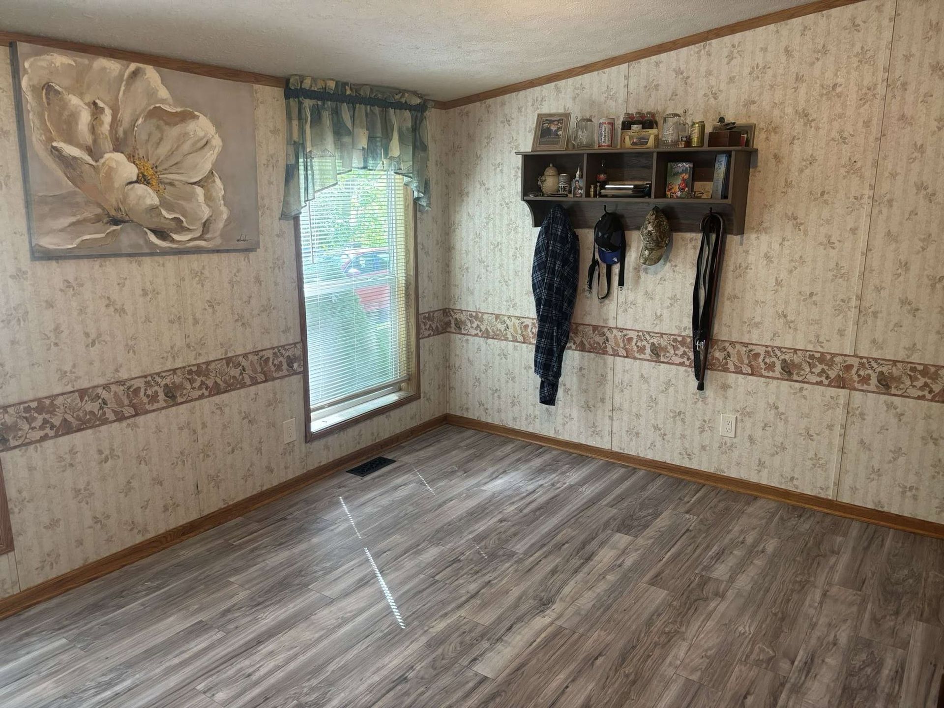 Empty room with wood-look floor, floral wallpaper, window, and coat rack with hanging clothes
