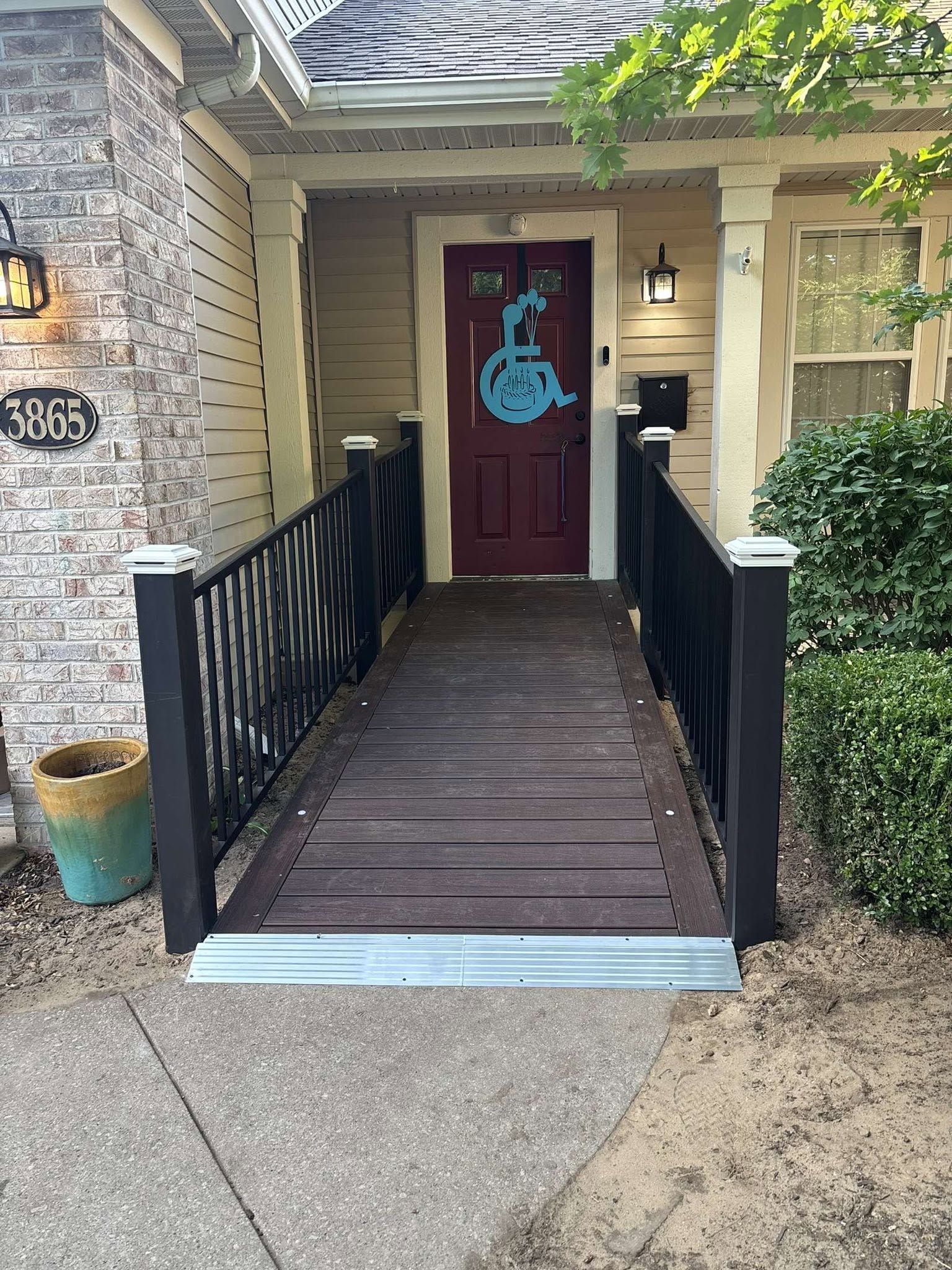 Front porch ramp leading to a red front door with a blue wreath, flanked by black railings.