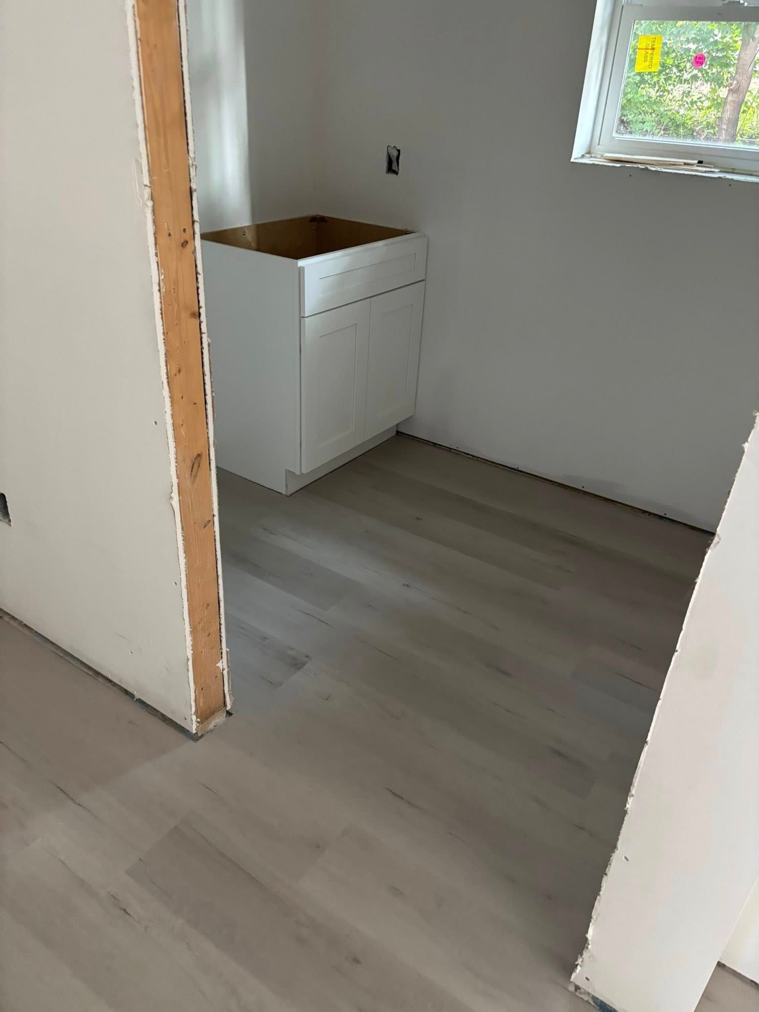 Empty room with white walls, gray flooring, and a small white cabinet beneath a window.