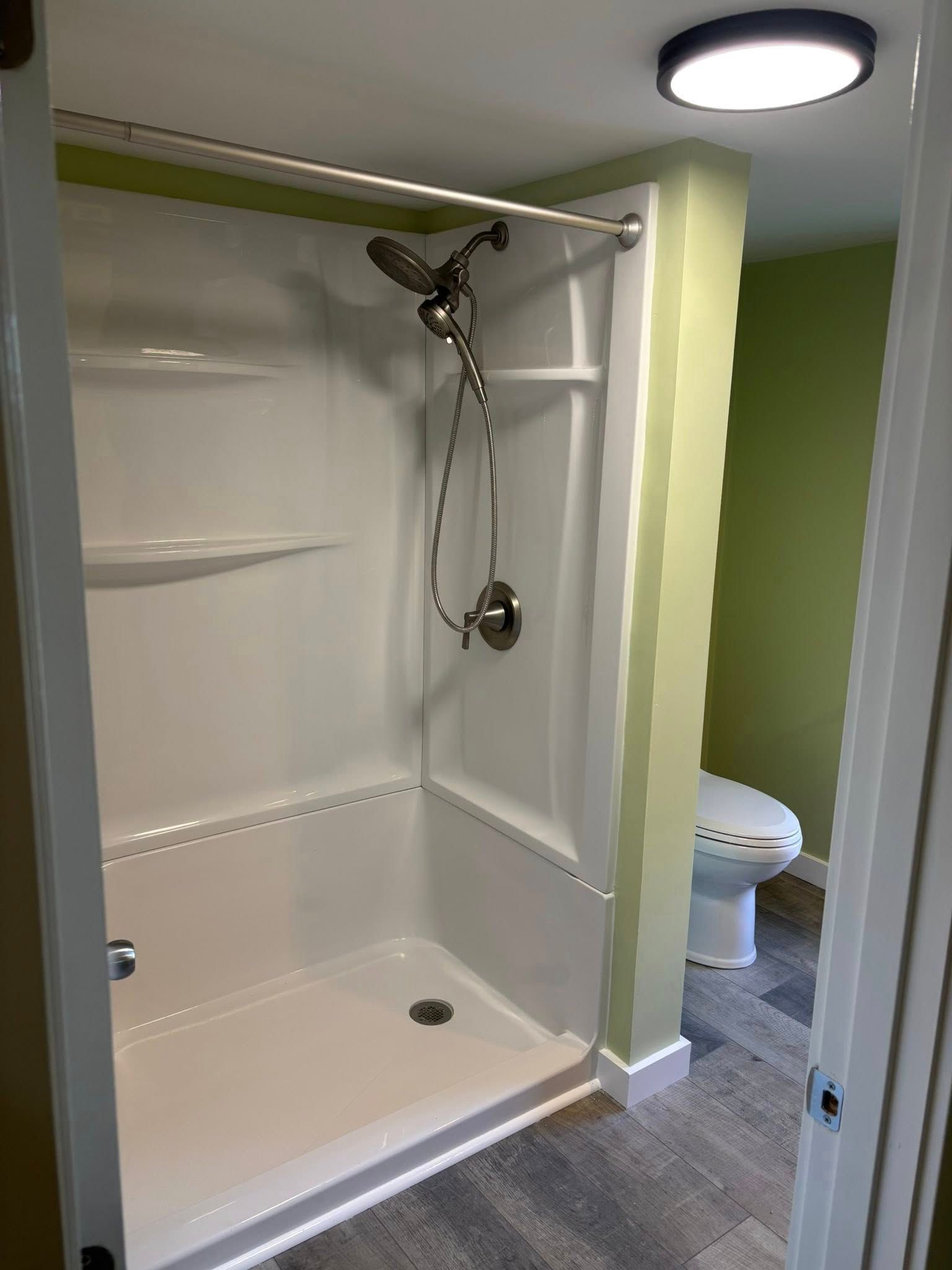 Small bathroom with a walk-in shower, white tile, chrome showerhead, and a toilet partly visible beyond the doorway.