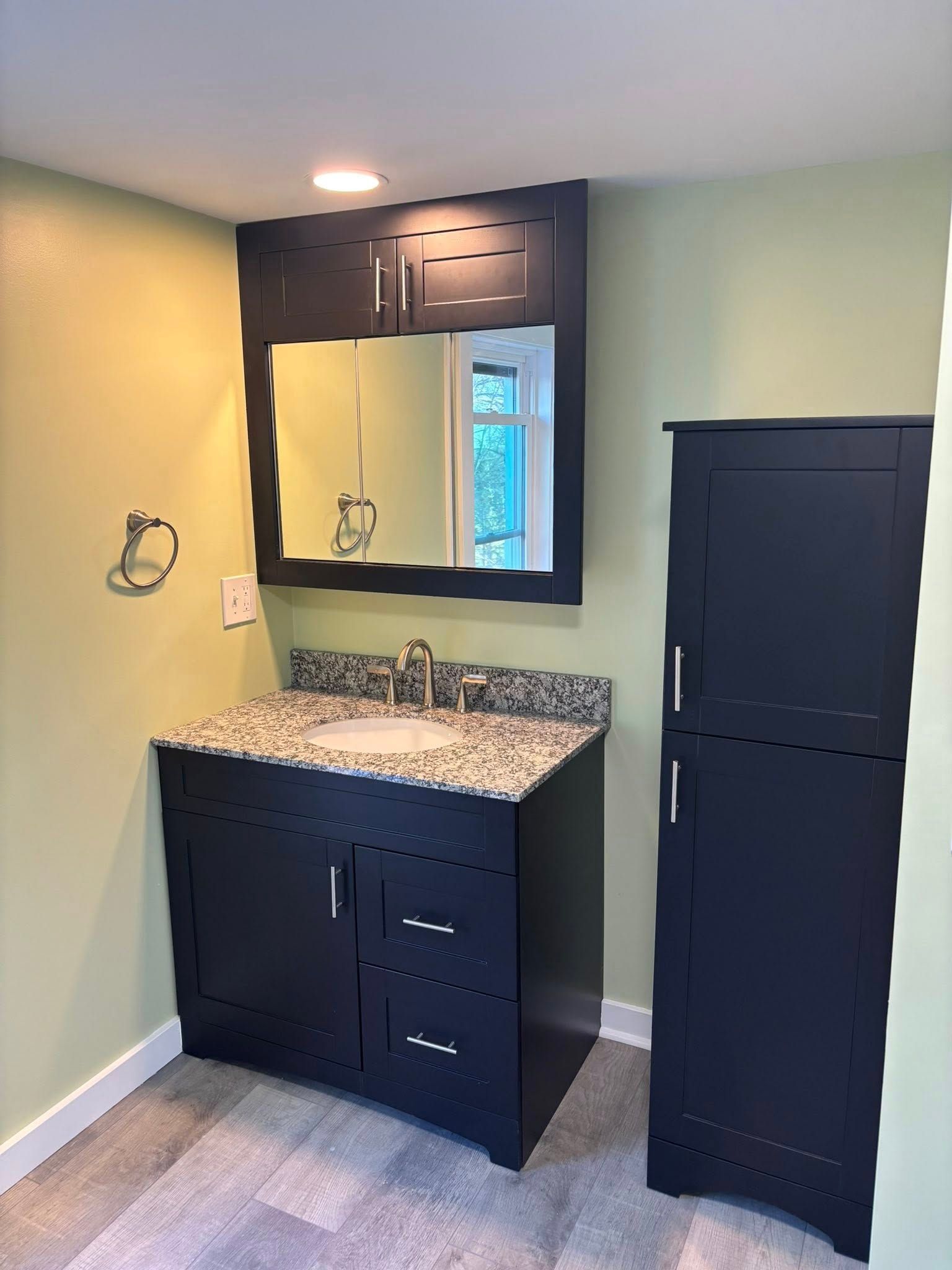 Small bathroom vanity with dark cabinets, granite countertop, mirror, and a tall black storage cabinet.
