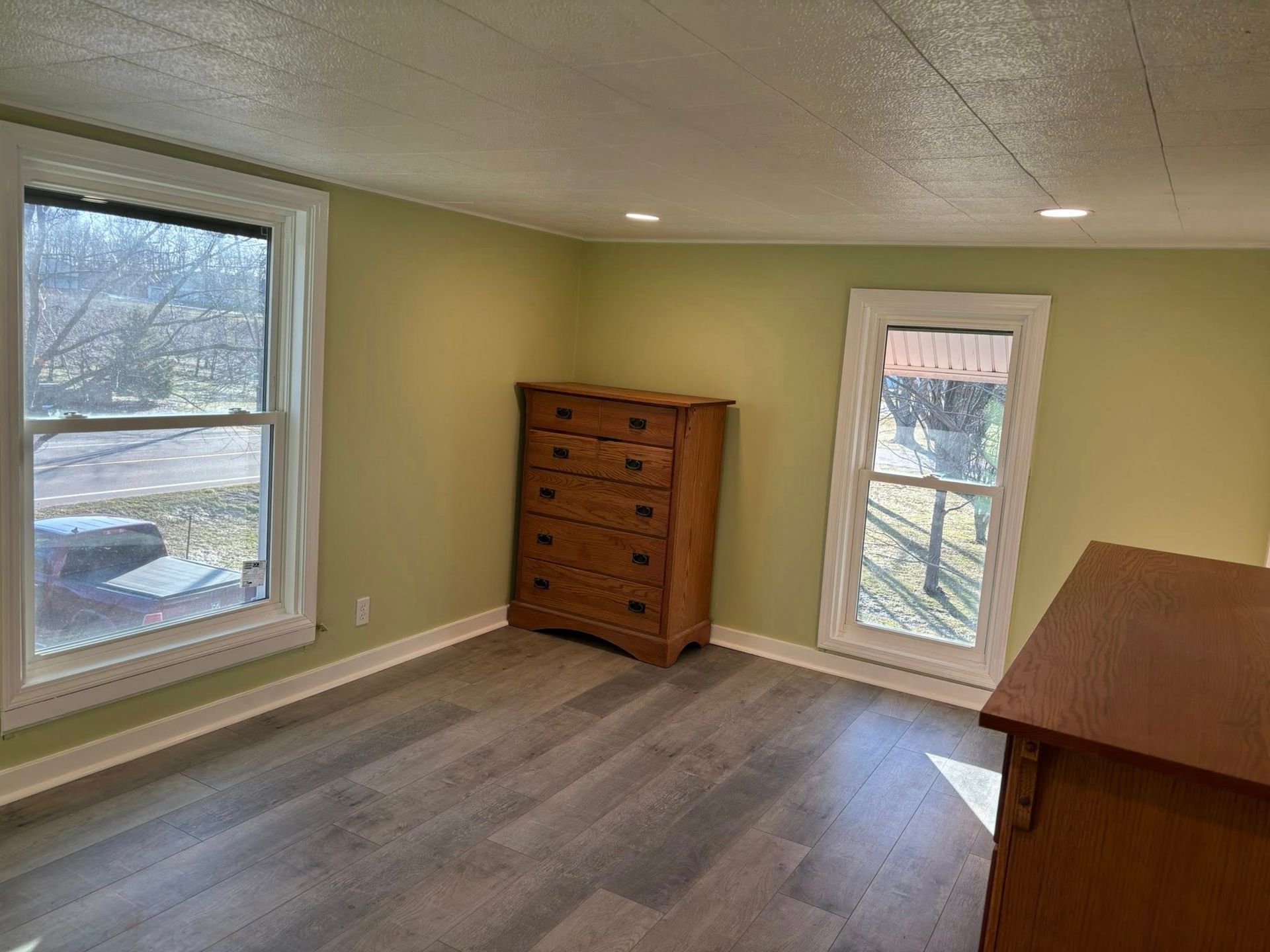Empty beige room with wood floor, window, dresser, and small door to outside