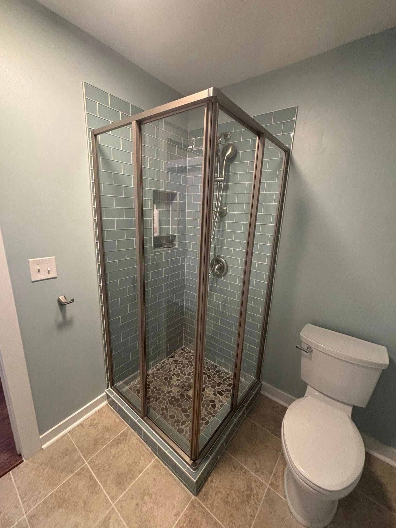 Corner bathroom with glass shower enclosure, beige tile floor, and toilet beside it.