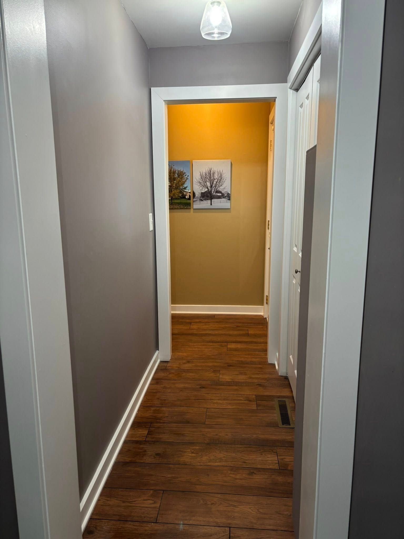 Narrow hallway with gray walls, wood floor, and a framed picture on a mustard-yellow accent wall.