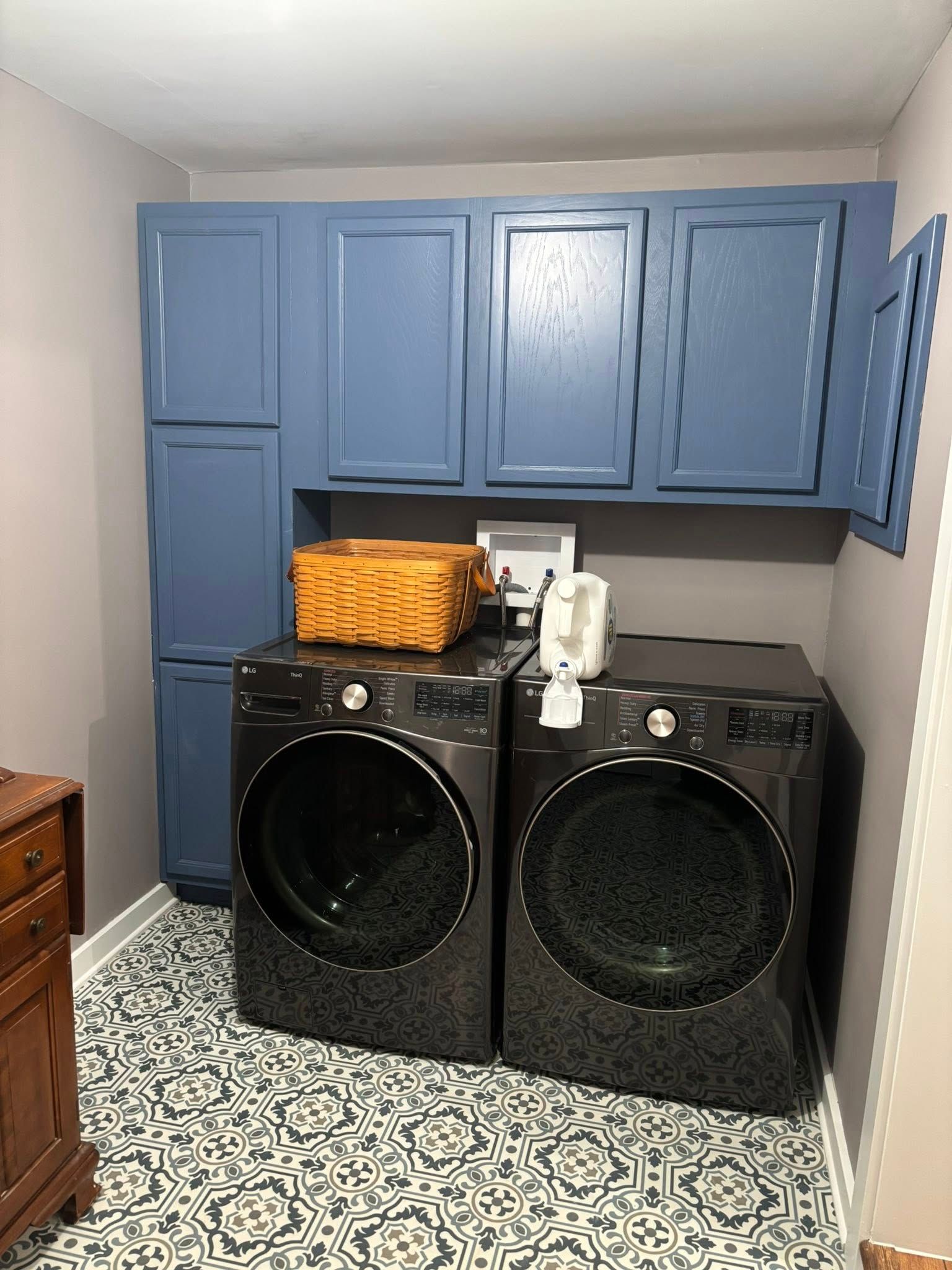 Laundry room with blue cabinets, a washer and dryer, wicker basket, and patterned floor.