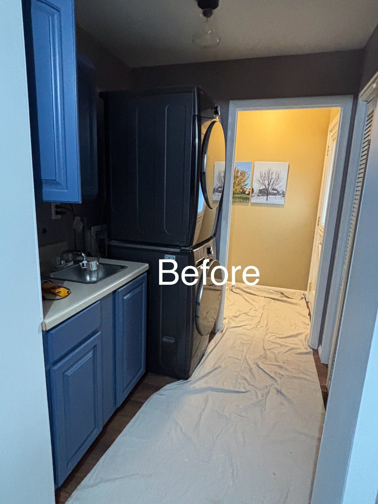 Narrow kitchen hallway with blue cabinets and a black refrigerator, labeled “Before” over a plastic-covered floor.