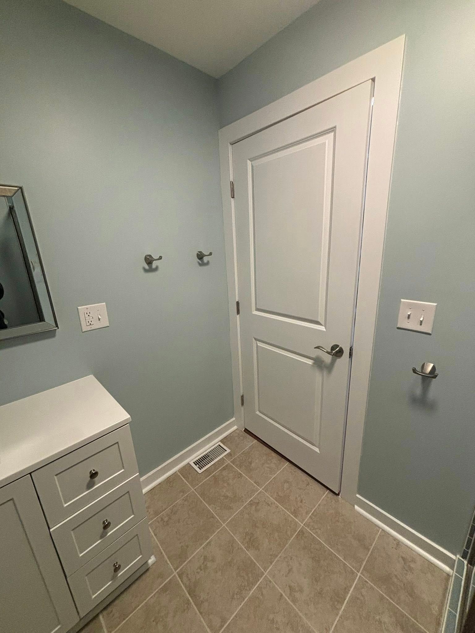 Small bathroom with gray walls, tiled floor, white door, and sink cabinet on the left.