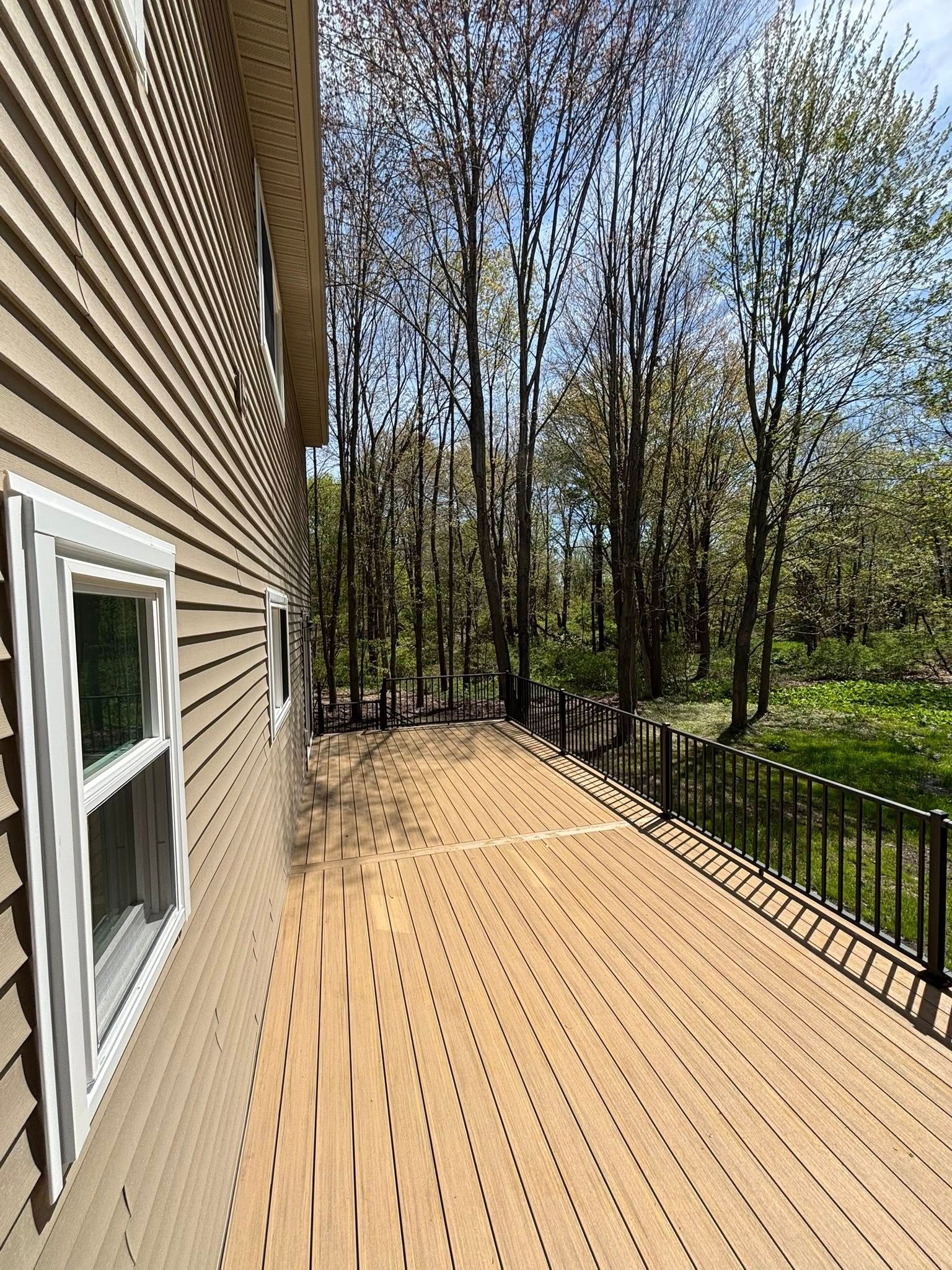 Wooden deck beside a house, with black railing and wooded backyard under a clear sky.
