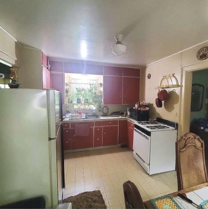 Small kitchen with red cabinets, white stove and fridge, sink under a window, and tiled floor.