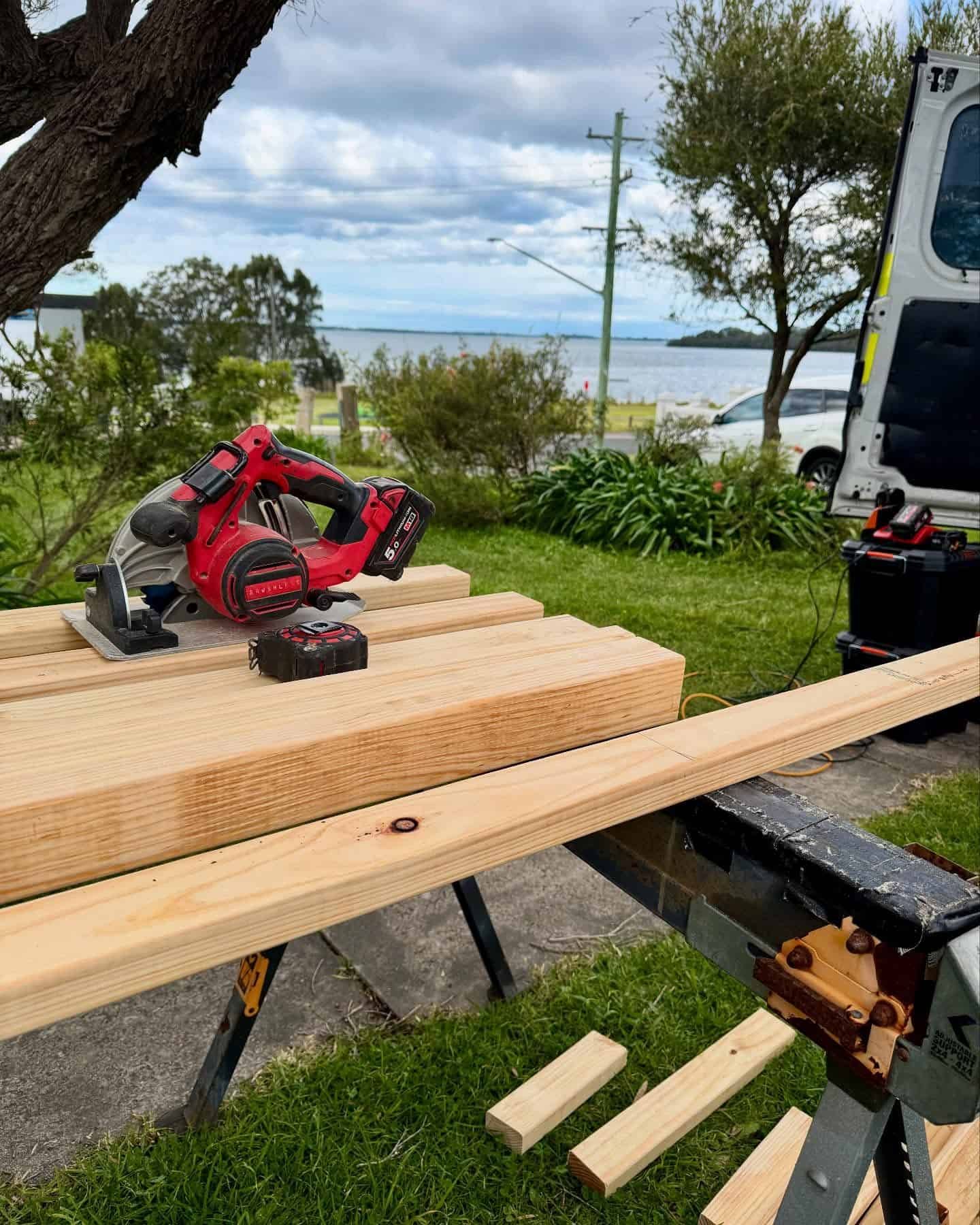 Red Circular Saw on Lumber at a Saw Horse Outdoors Near a Van and Waterfront — Catios By Paulie in Wollongong, NSW